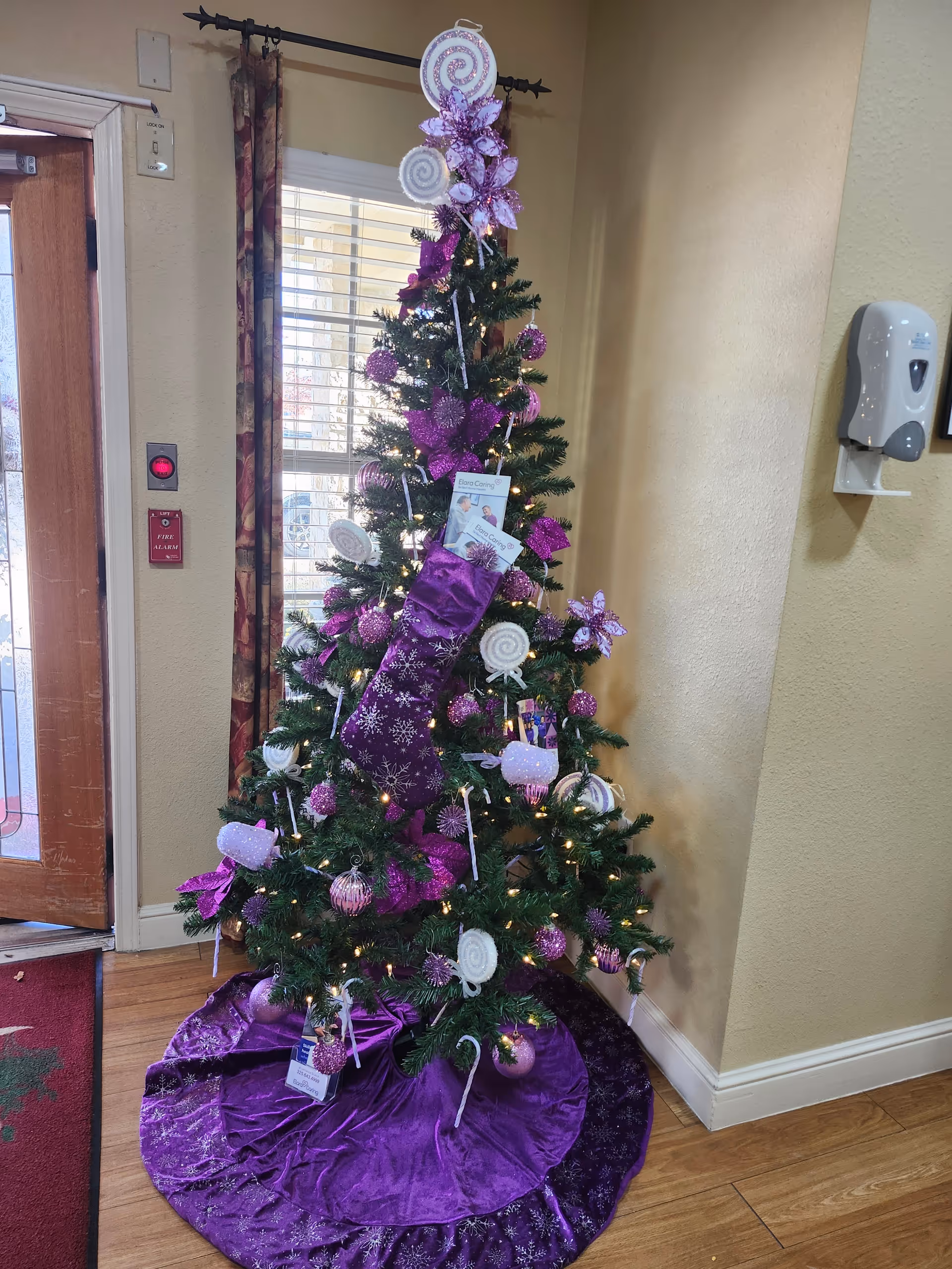 An indoor Christmas tree decorated in purple, placed in a hallway of a senior living facility.