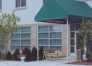 Exterior view of Mercyhealth Hospice Wisconsin entrance with a green canopy and outdoor seating.