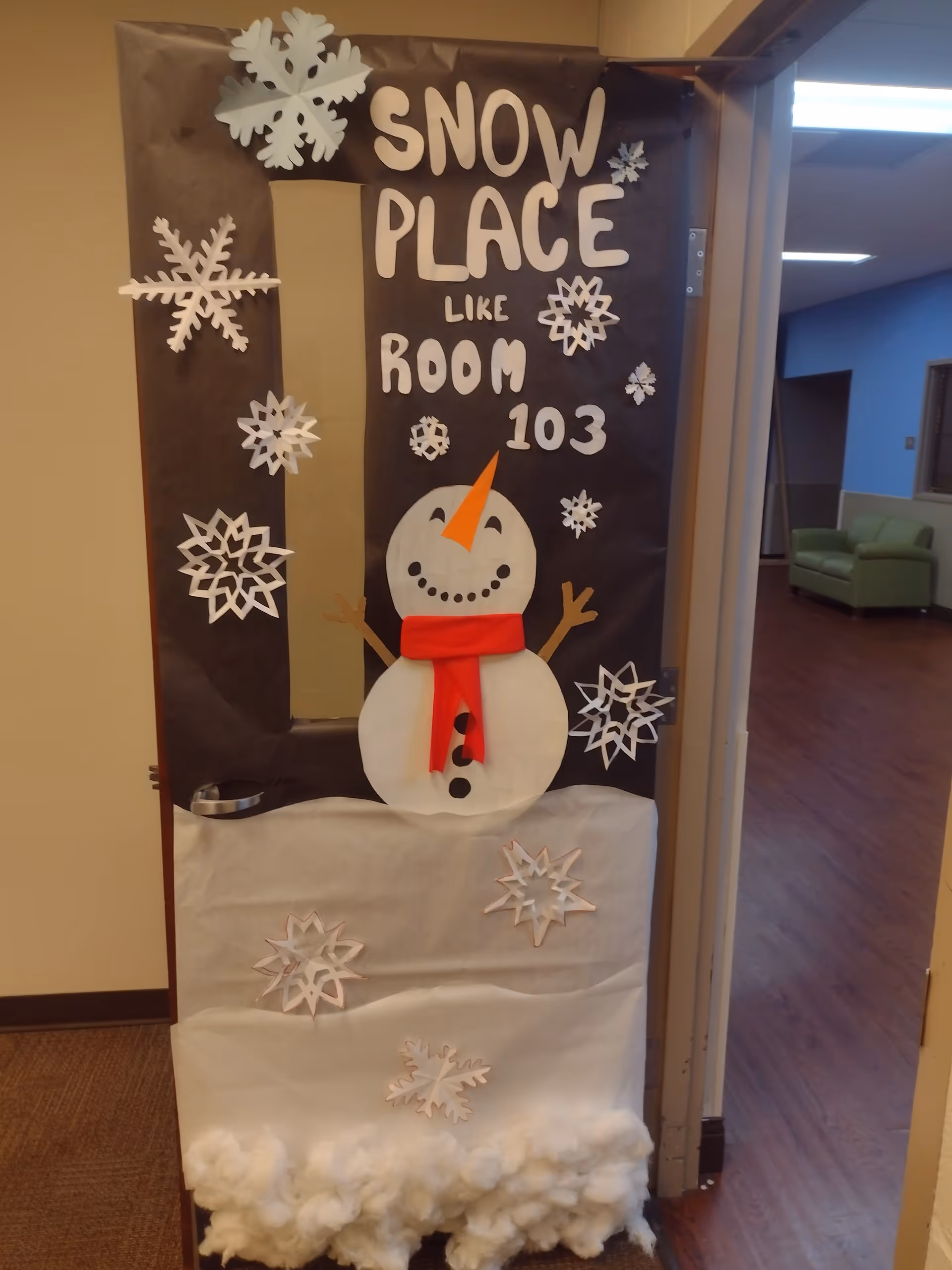 Decorated doorway featuring a snowman, snowflakes, and Snow Place Like Room 103 in a hallway.