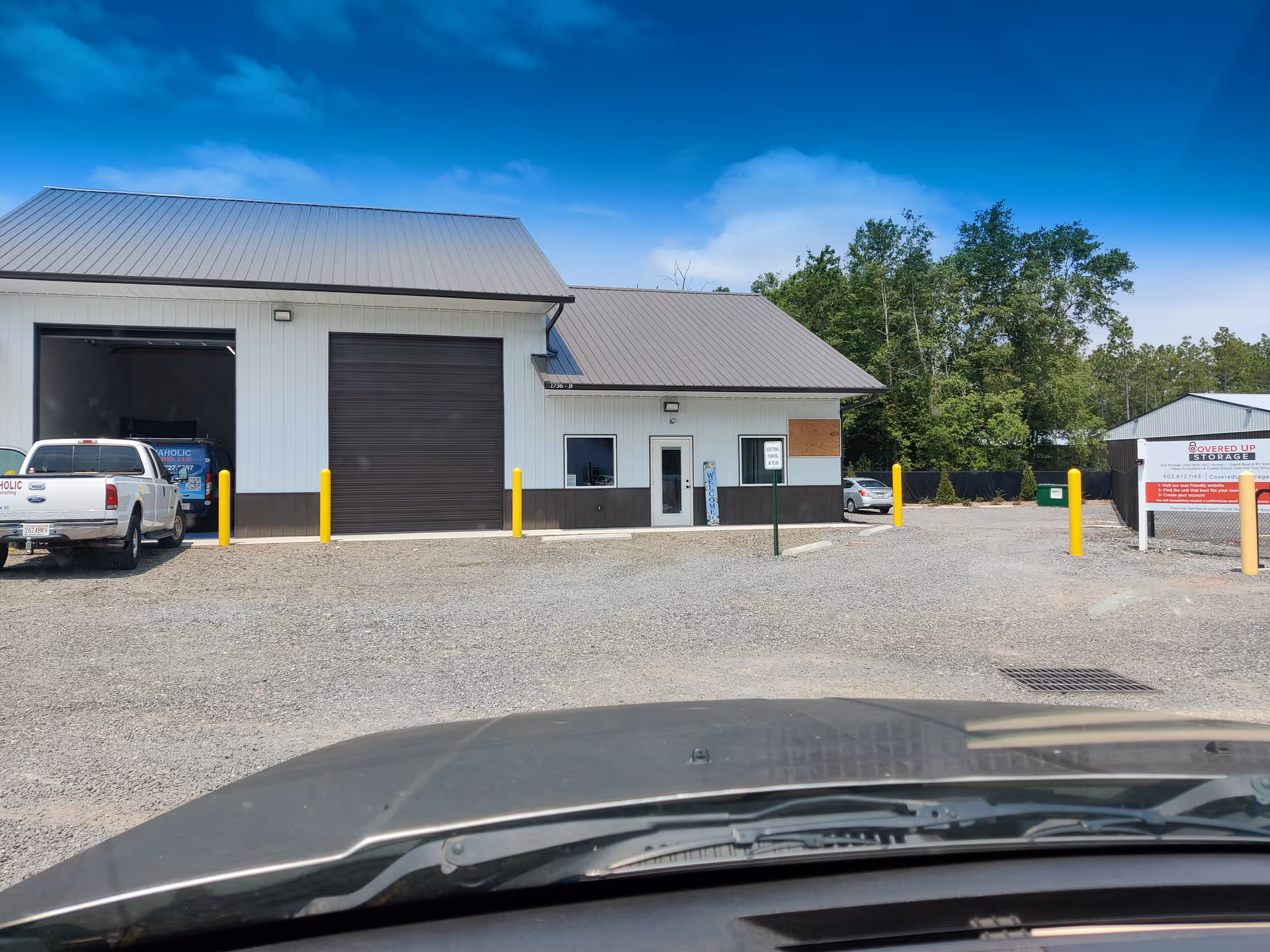 Exterior view of a light-gray building with a large garage door and pickup truck.