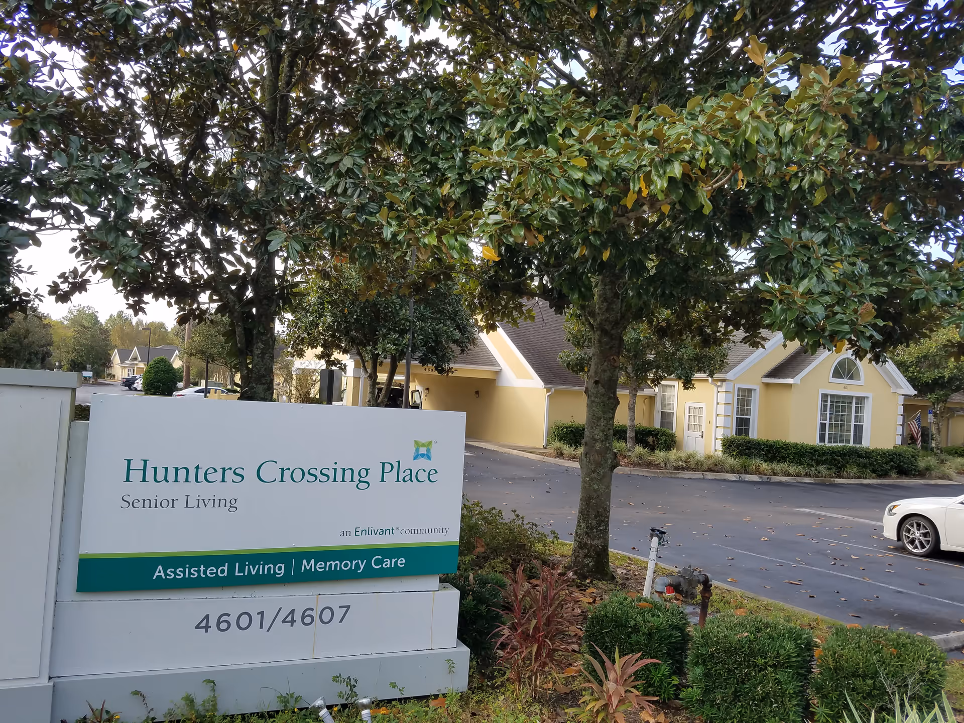 Yellow building of Hunters Crossing Place Senior Living with a front sign and trees