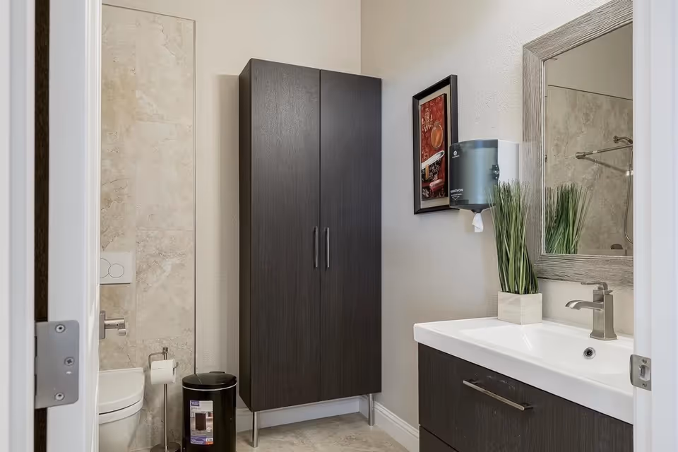 Modern bathroom in a senior living facility with sink, cabinet, mirror, and toilet.