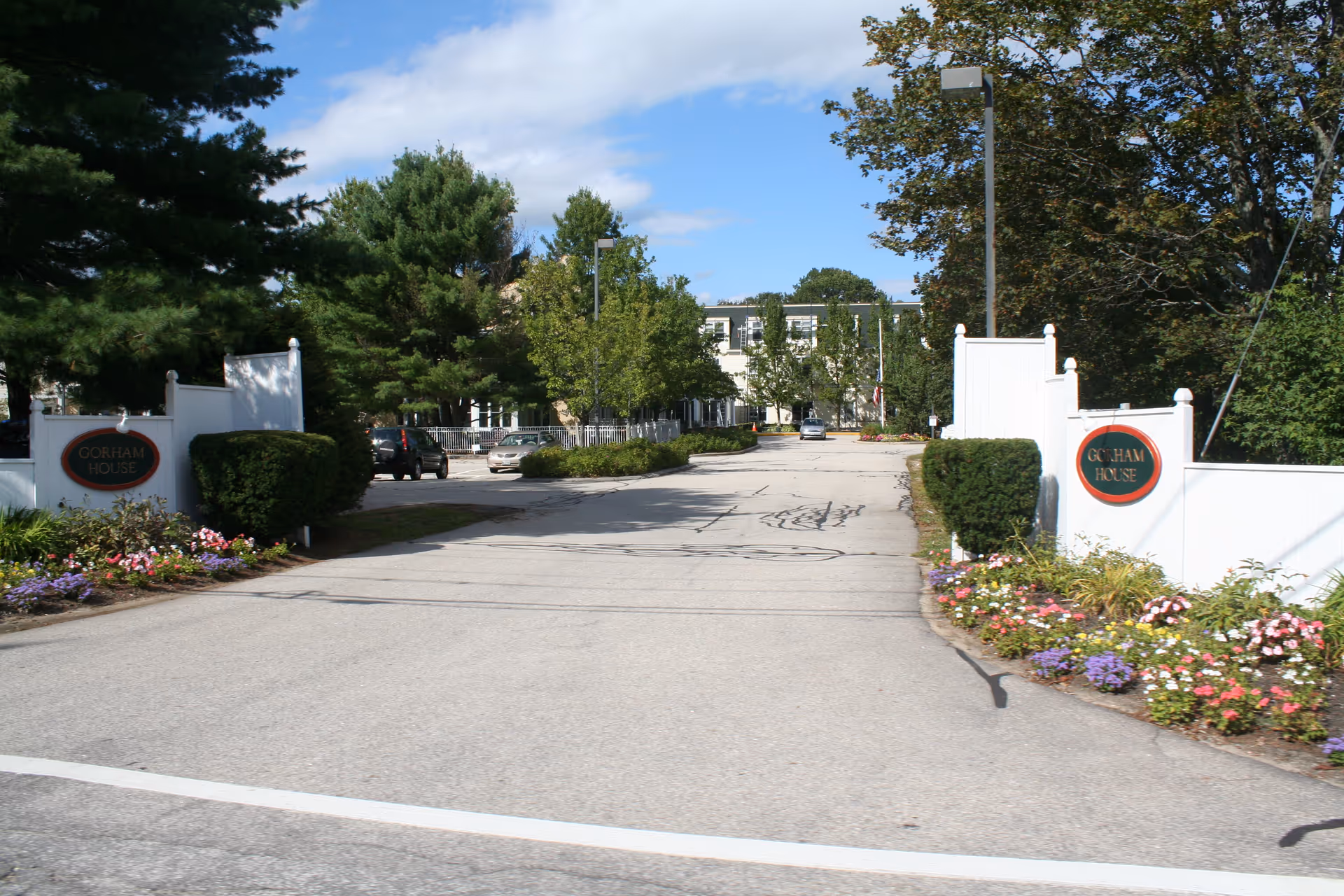 Entrance road to Gorham House senior living, white gates, manicured shrubs, colorful flowers