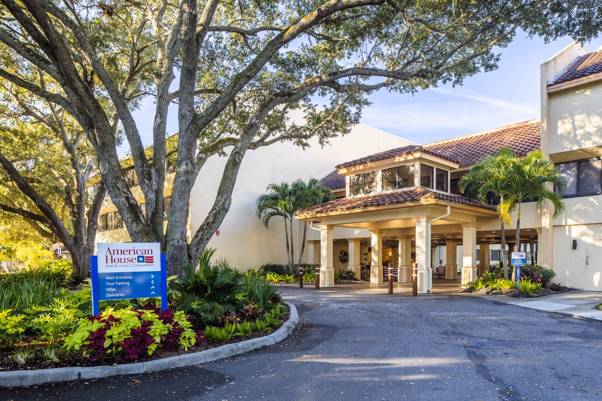 Exterior view of American House Sarasota entrance with a porte-cochère and landscaping.