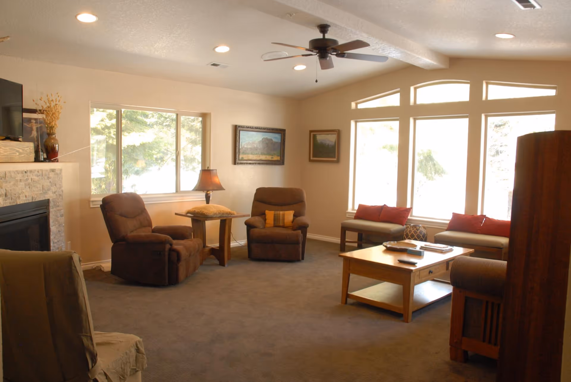 A cozy senior living living room with recliners, a sofa, coffee table, fireplace, and large windows.