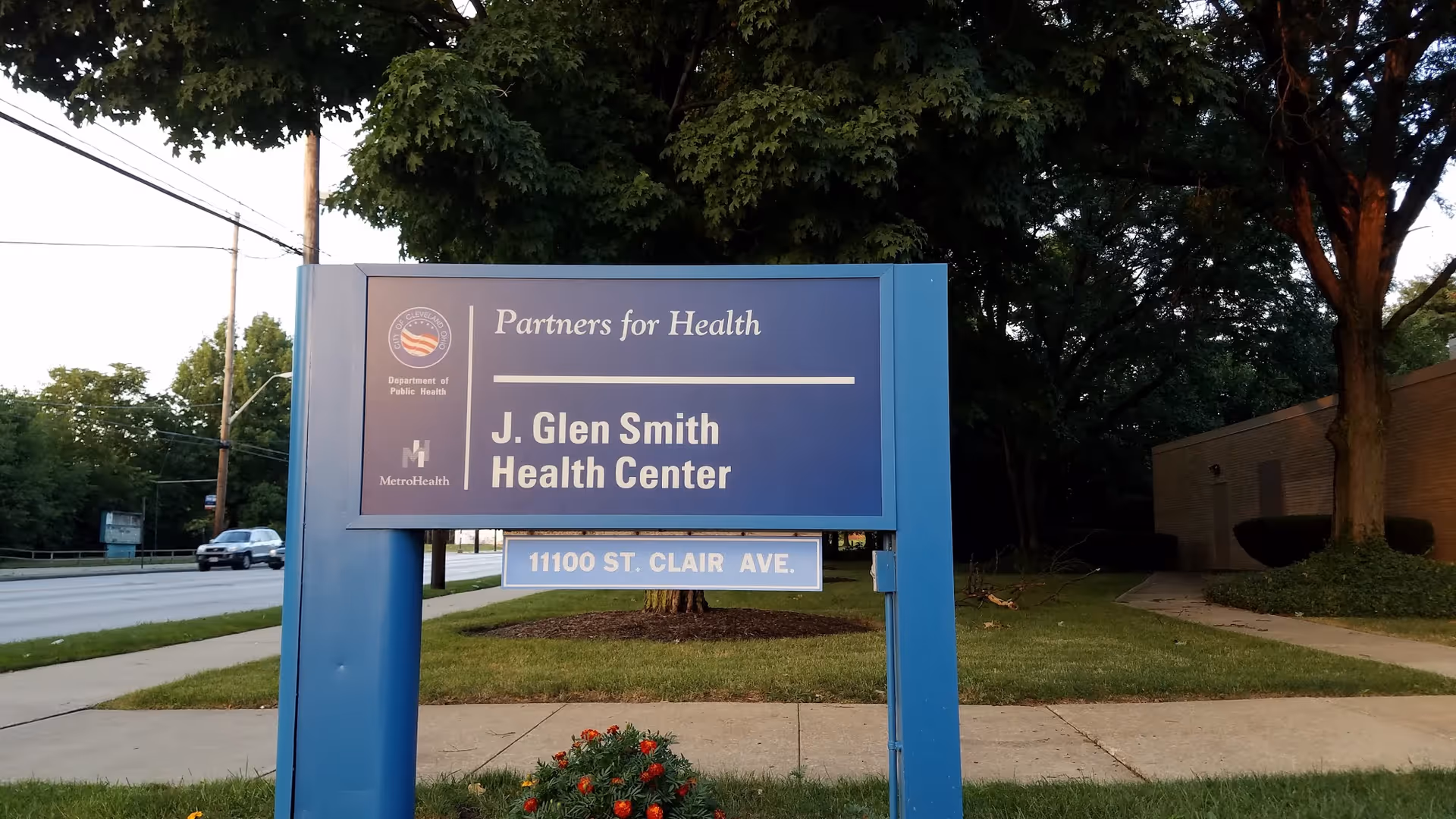 Blue outdoor sign for J. Glen Smith Health Center with street and trees in background.