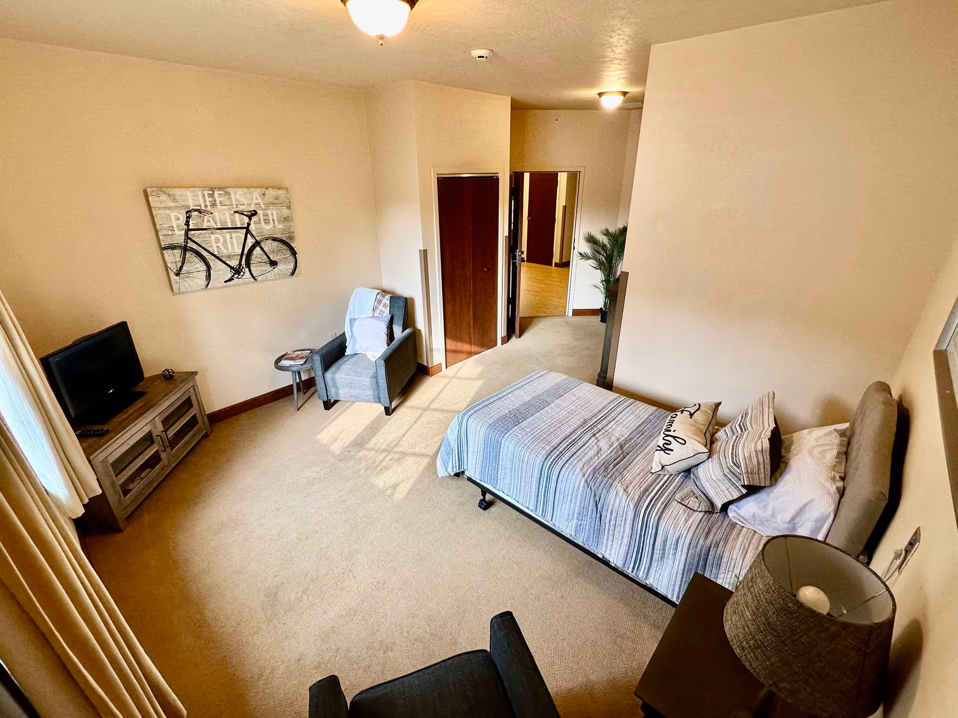 Bedroom in a senior living facility with bed, seating area, and TV.