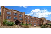 Brick three-story Good Shepherd Nursing Home exterior with entrance steps and blue sky.