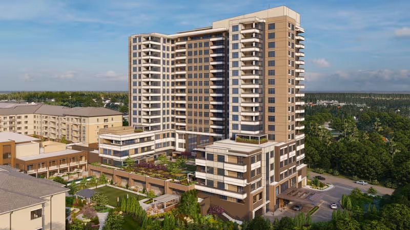 Aerial view of a large multi-story senior living facility named The Cardinal at North Hills, featuring a tall central building with balconies, surrounded by landscaped gardens, outdoor seating areas, and additional lower-rise buildings, set against a backdrop of trees and a partly cloudy sky.