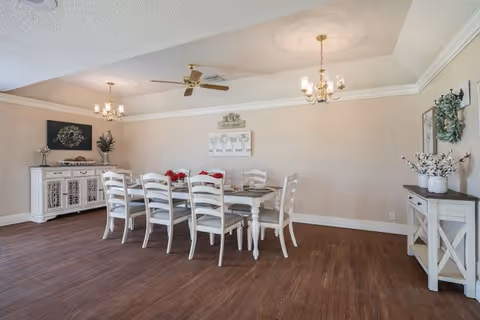 Bright dining room with a long white table, chairs, overhead chandelier, and sideboard.