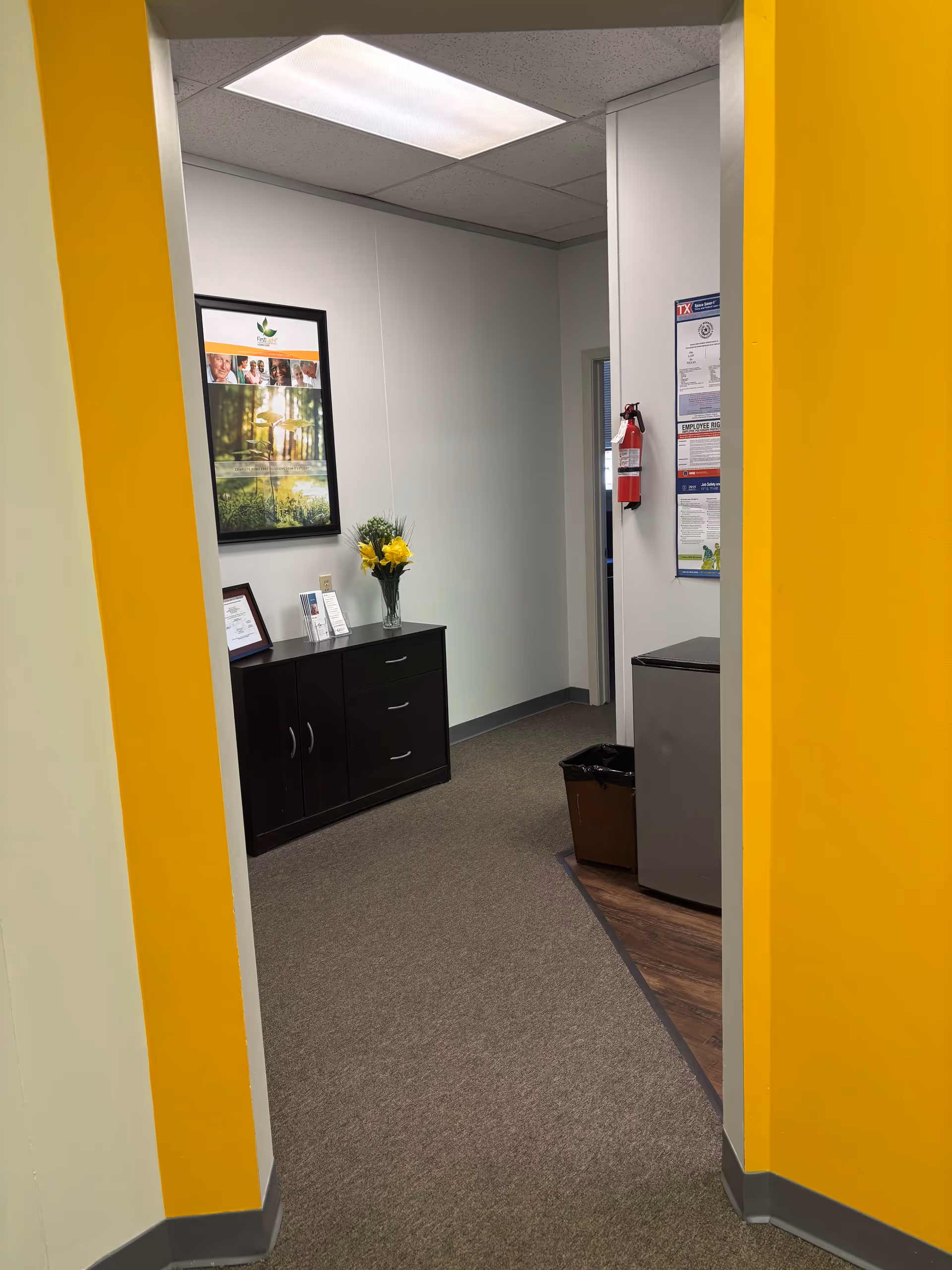 Bright indoor hallway with yellow walls, a small office area, and a cabinet.