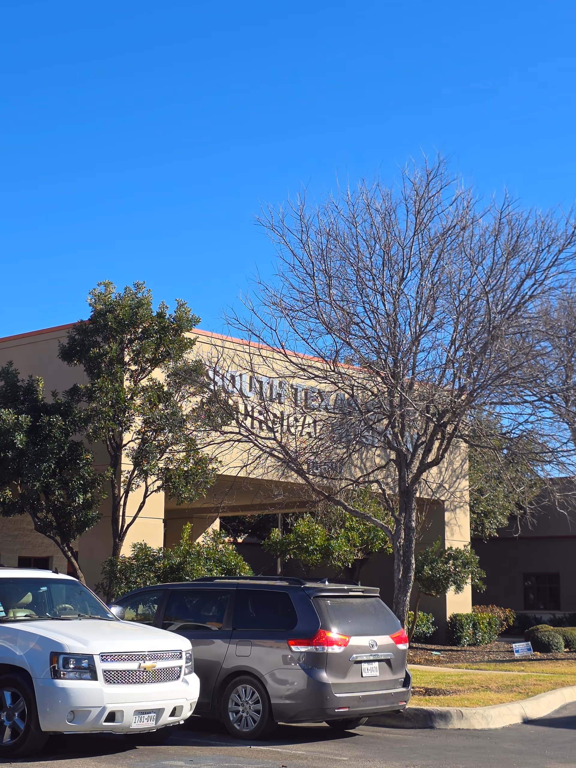 Front view of South Texas Spine and Surgical Hospital with parked cars and blue sky.
