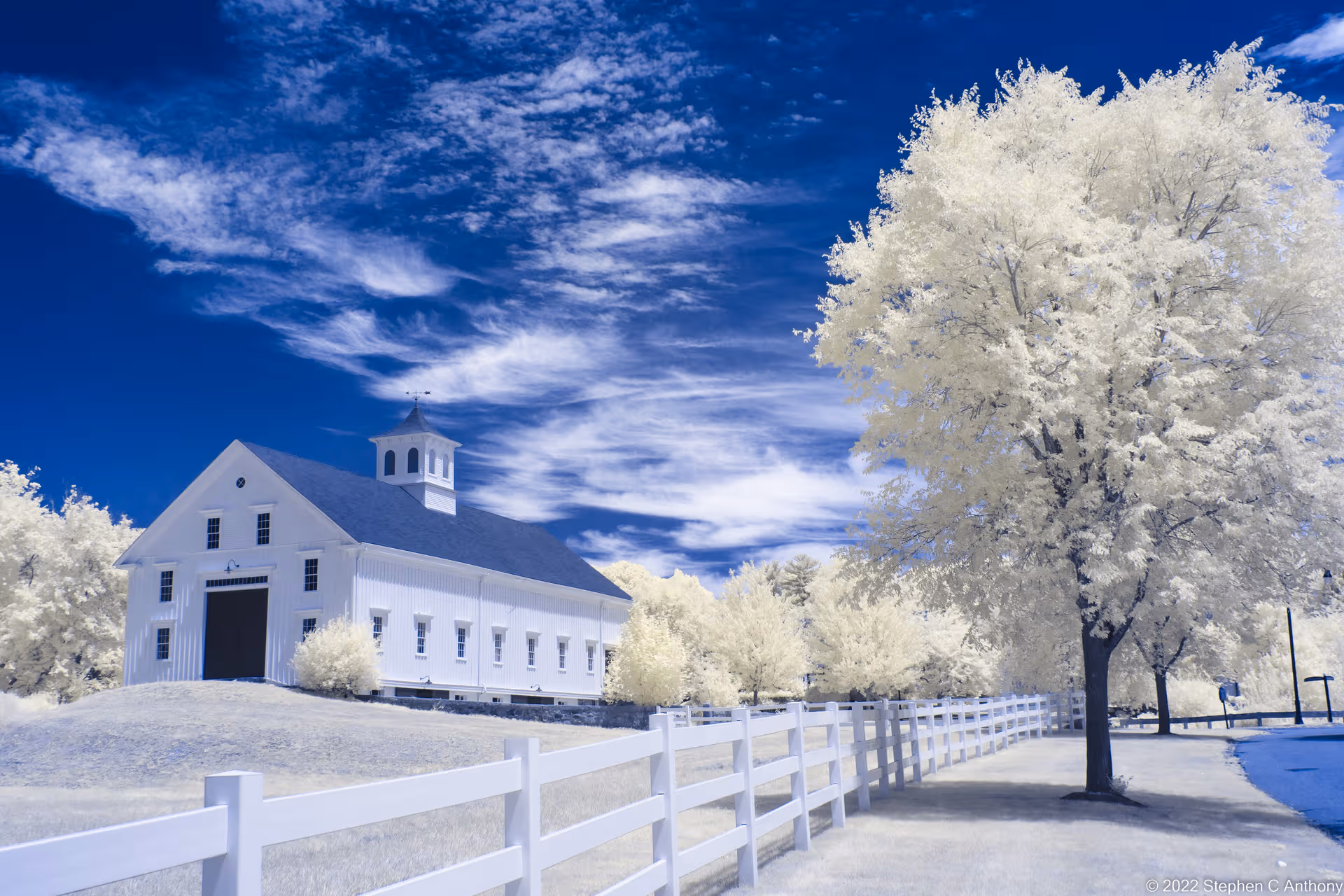White community building with a cupola, fence, and trees beneath a blue sky.