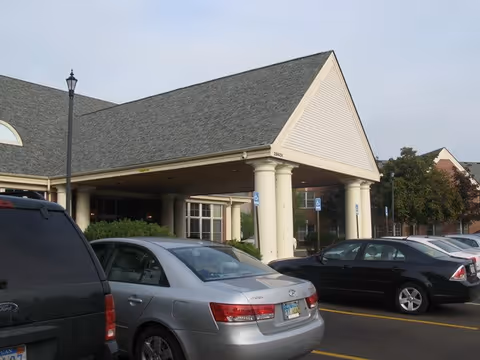 Covered porte-cochere entrance of a senior living facility with parked cars in front.