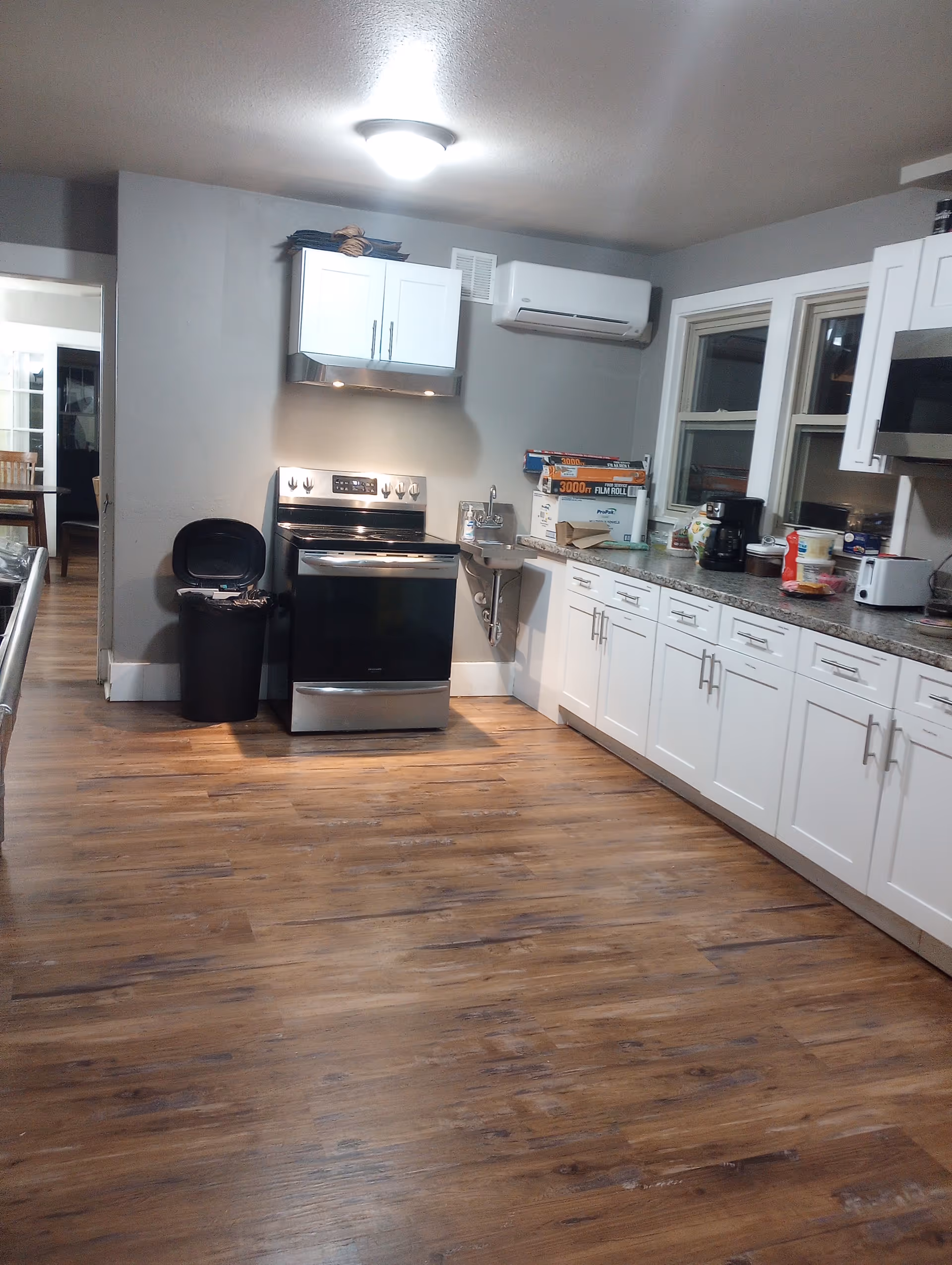 Bright kitchen with white cabinets, stainless steel stove, and wooden flooring in a senior living unit.