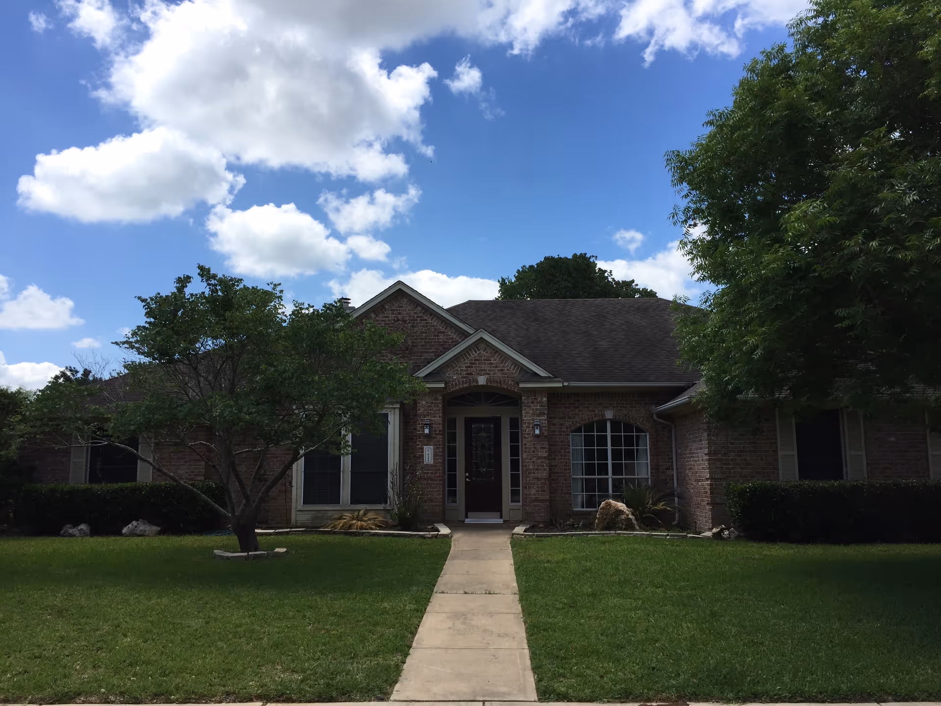 Brick, single-story building with a central entrance, surrounded by a green lawn and trees.