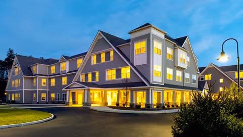 Large multi-story senior living facility with warmly lit entrance at dusk.