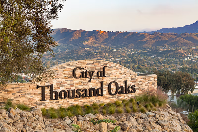 Stone sign reading City of Thousand Oaks set on a rocky hillside with mountains.