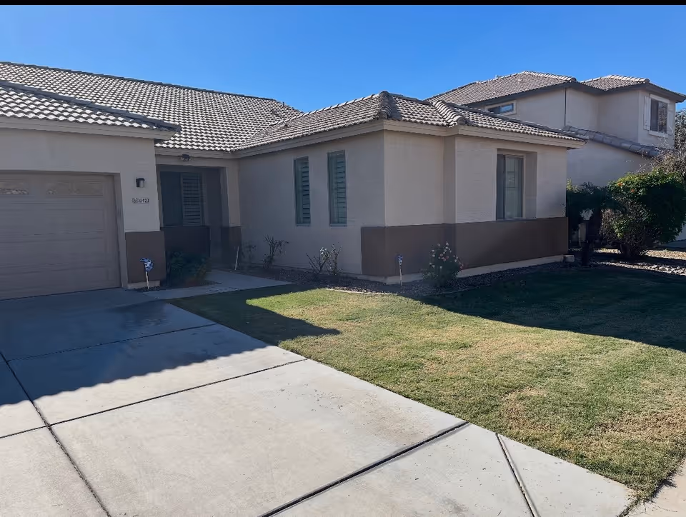 Front exterior of a beige, single-story residence with driveway and manicured lawn.