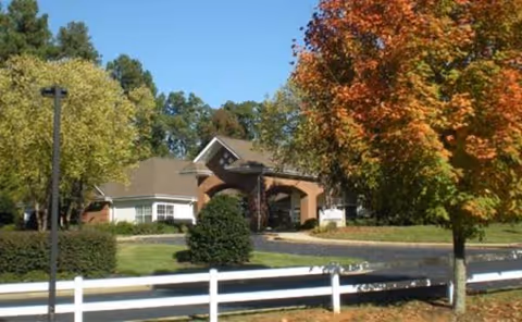Exterior view of Carriage House Senior Living Community entrance with trees and a white fence.