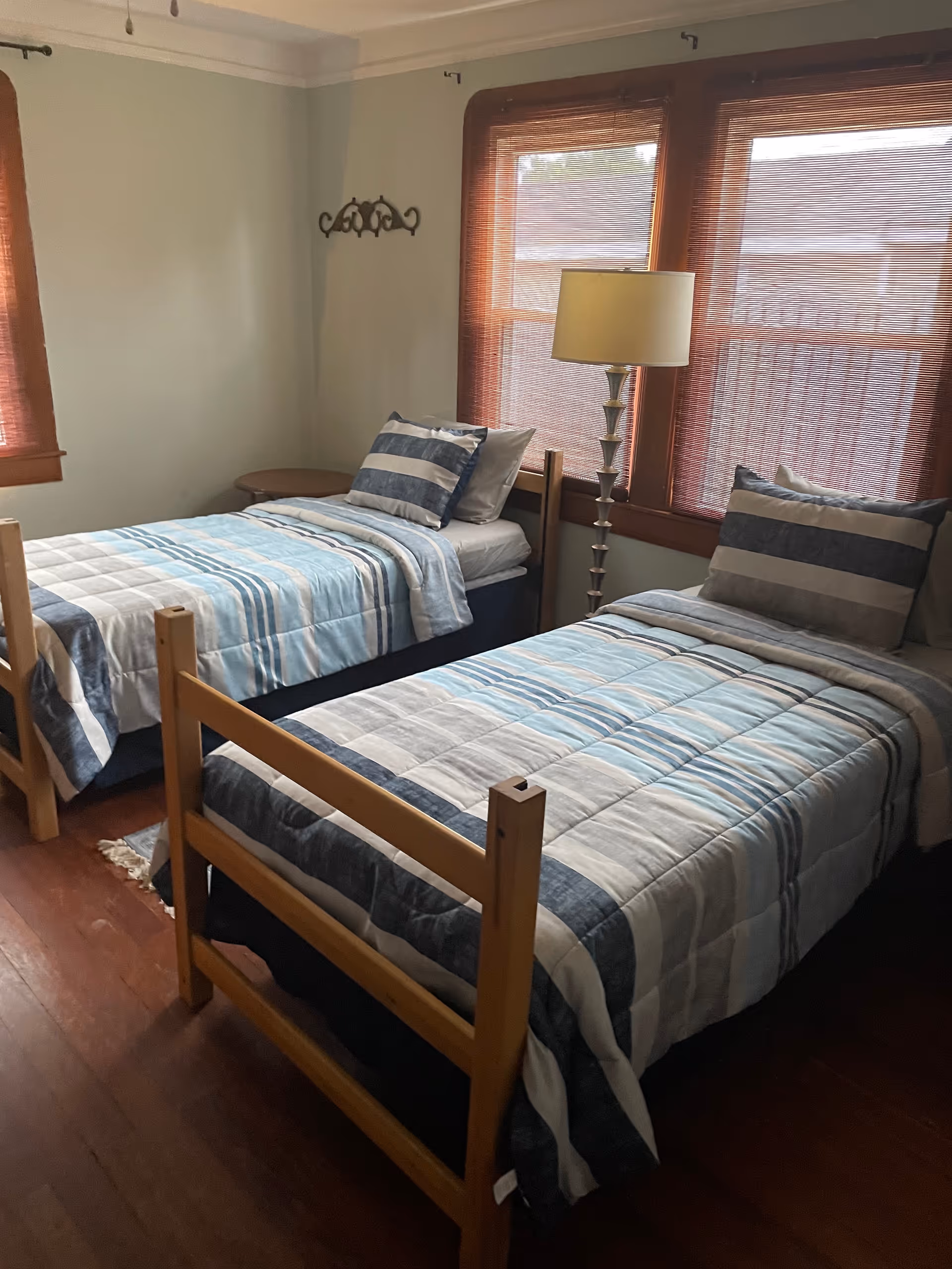 Two twin beds with blue striped bedding fill a small, sunlit bedroom.
