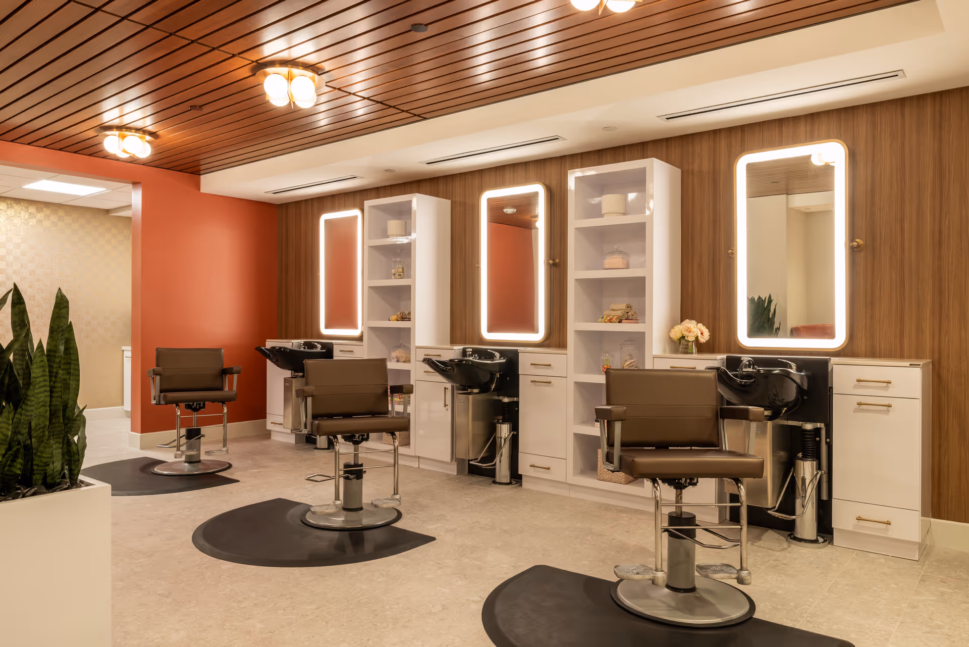 Hair salon area with styling chairs, sinks, and illuminated mirrors along wood paneling.