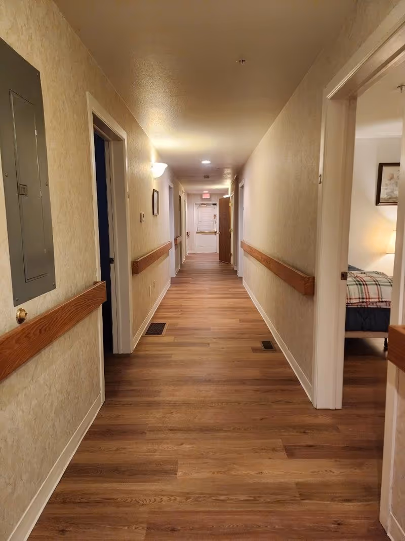 Long hallway inside a senior living facility with doors, handrails, and wood-style flooring.