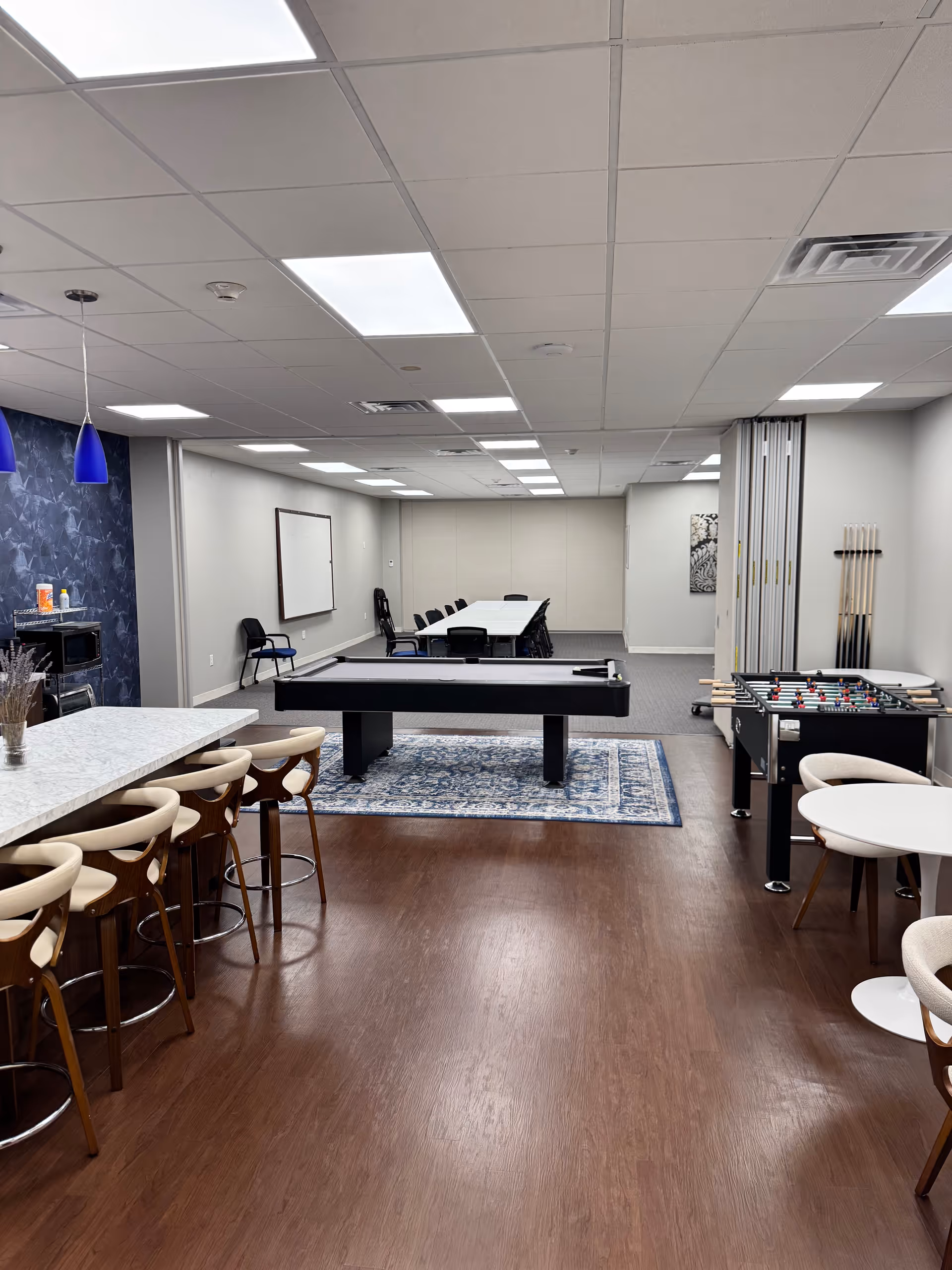 Empty senior living facility common room with a pool table, foosball, bar stools, and seating.