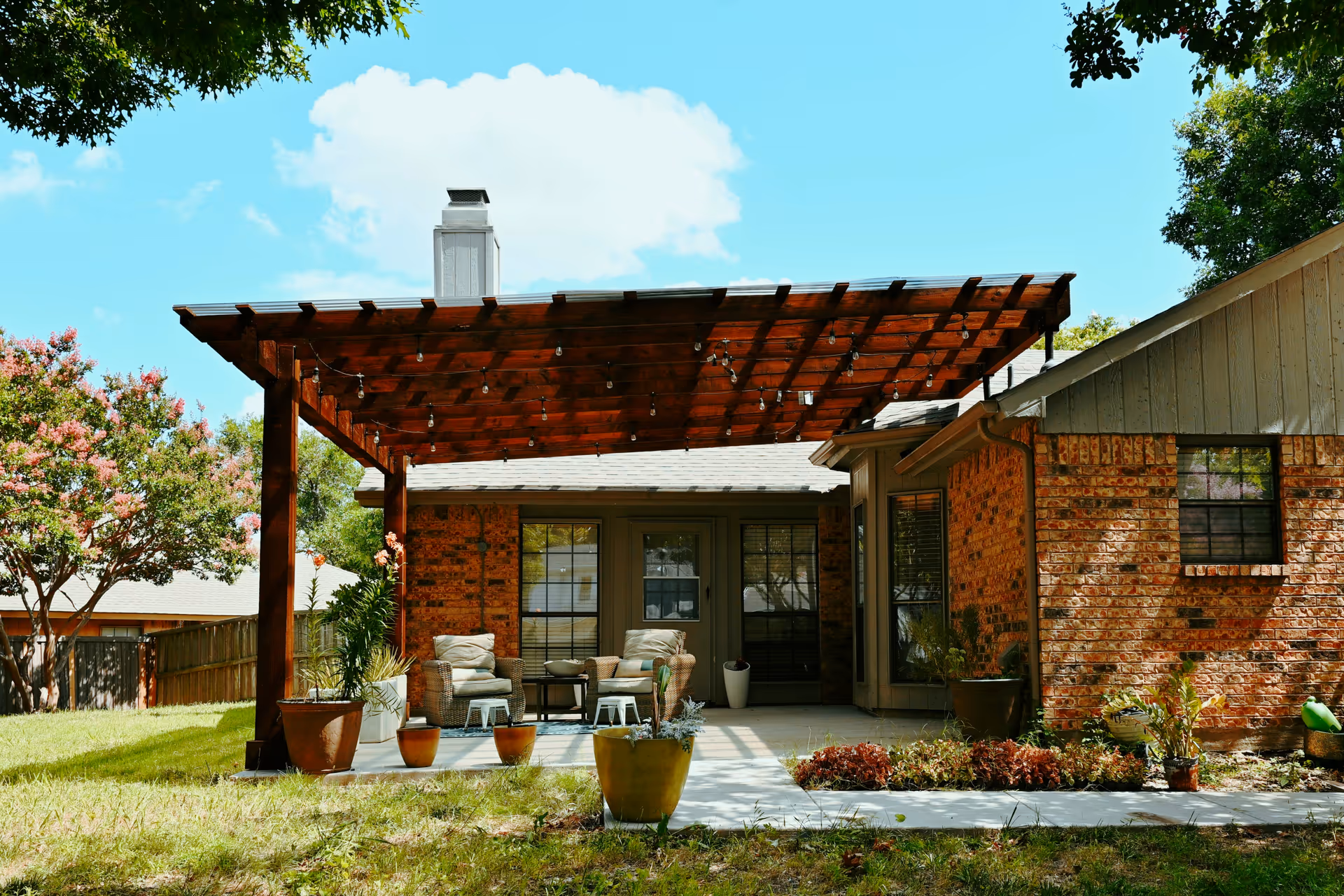 Brick building with wooden pergola patio and garden chairs outdoors.