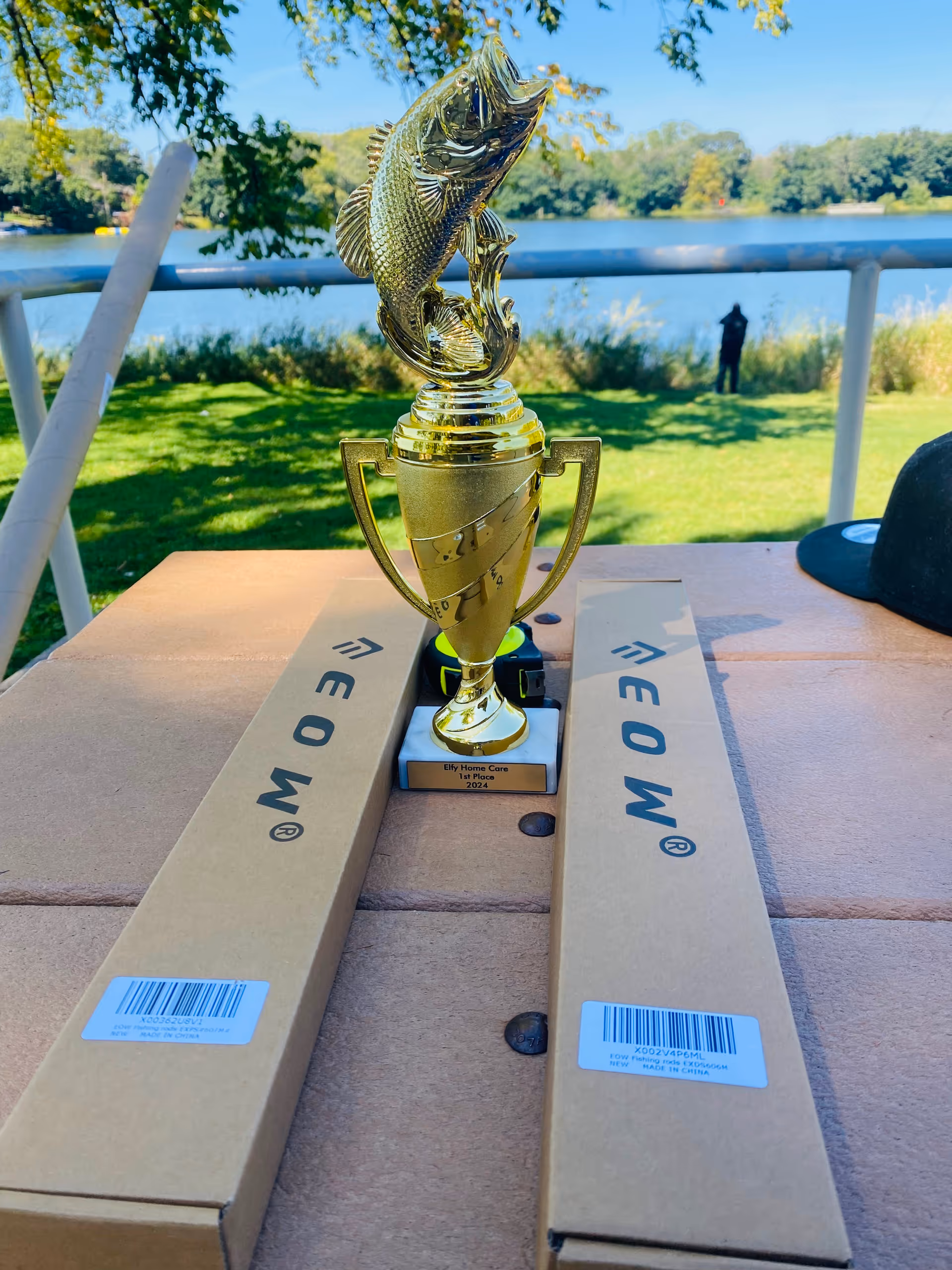 Golden trophy on a table outdoors near a lake, flanked by two long boxes.