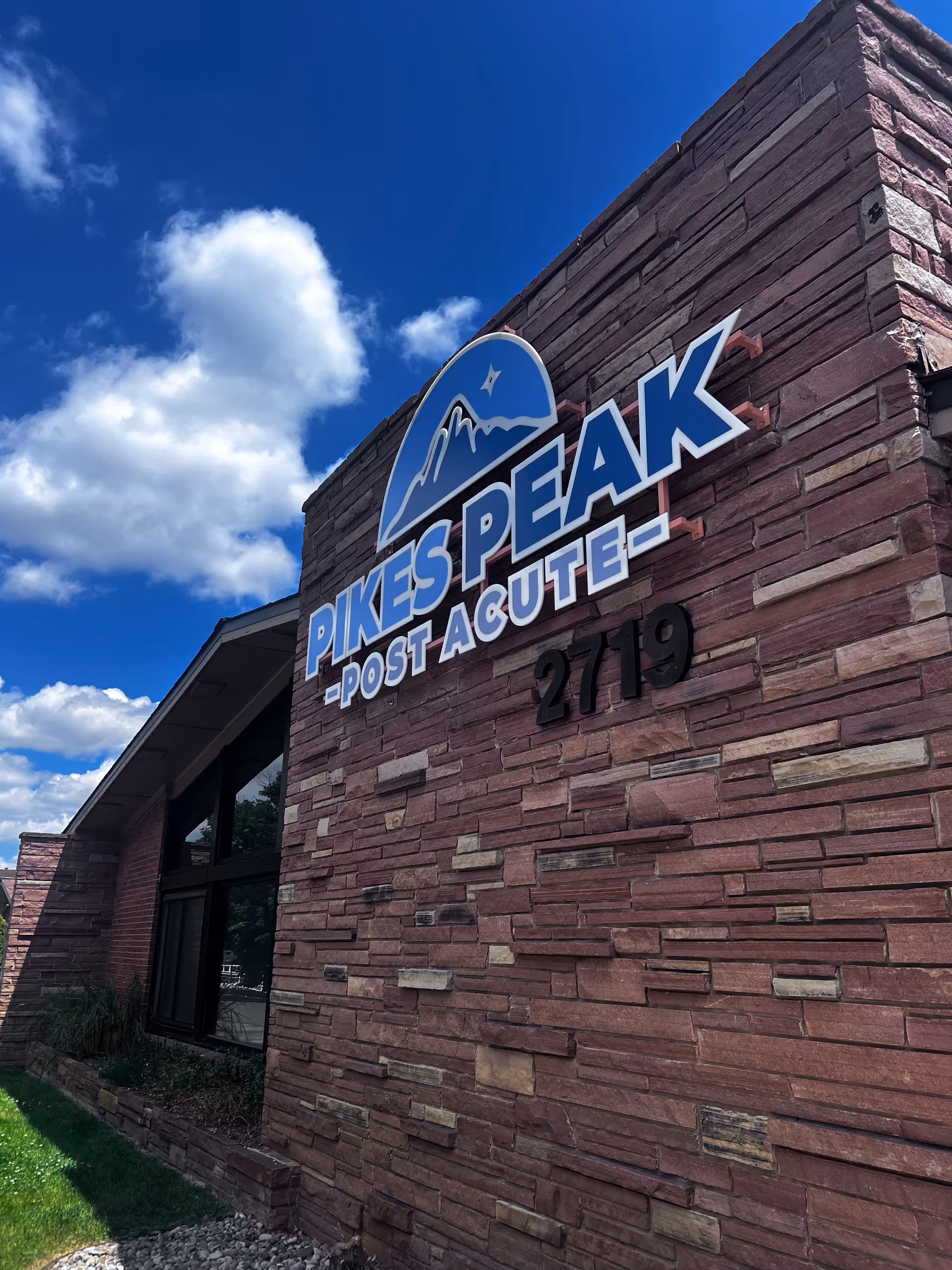 Exterior view of Pikes Peak Post Acute facility with brick wall and sign.