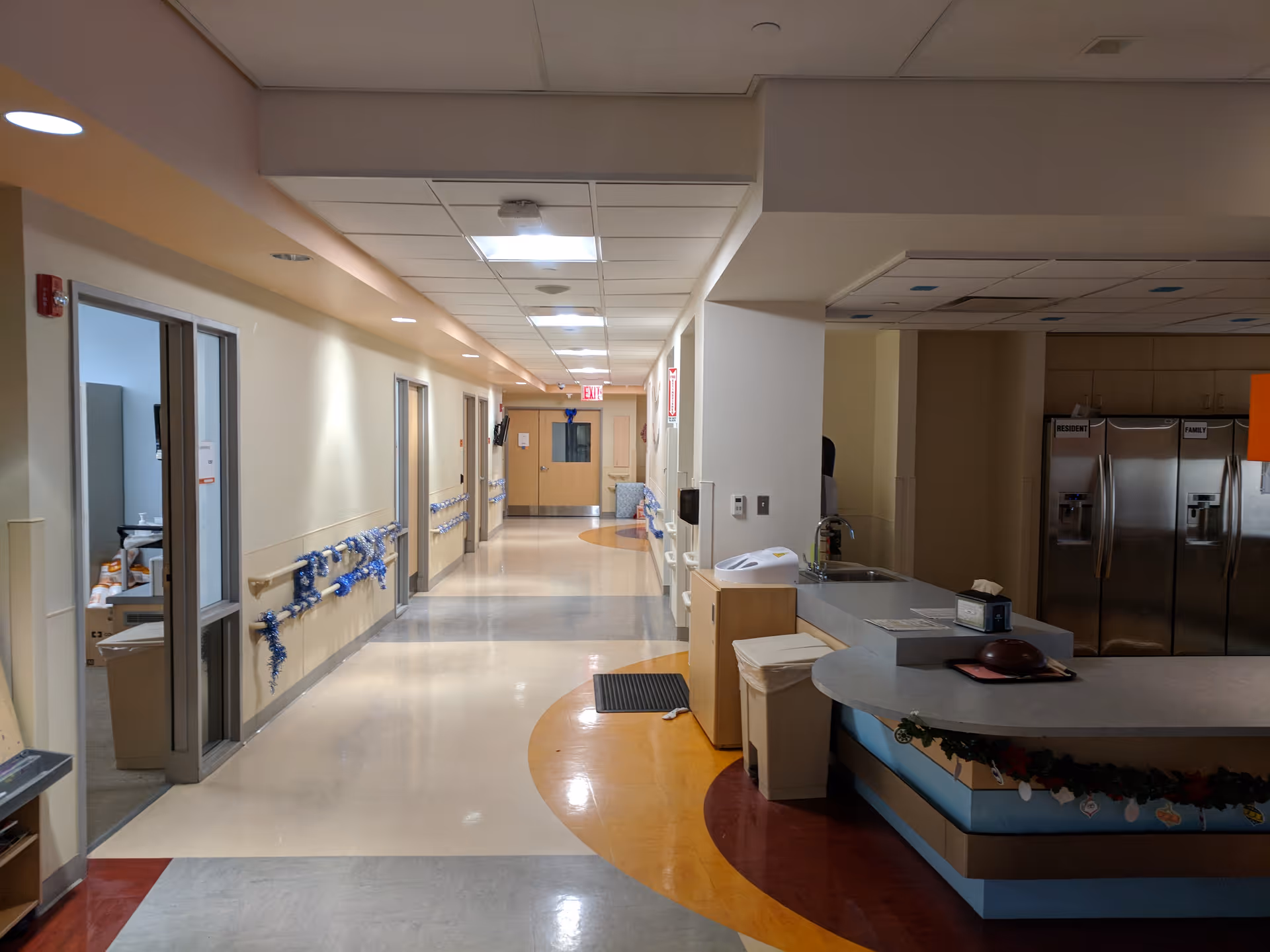 Wide hospital corridor with a curved reception desk on the right and doors along the left.