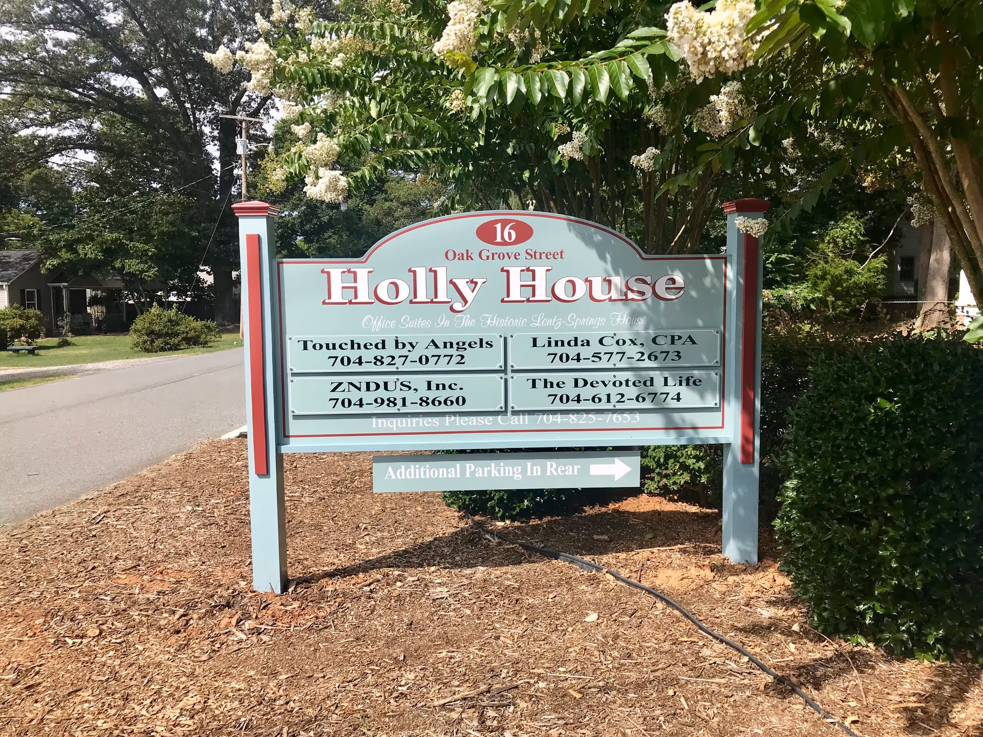 A large sign for Holly House office suites on a tree-lined street.