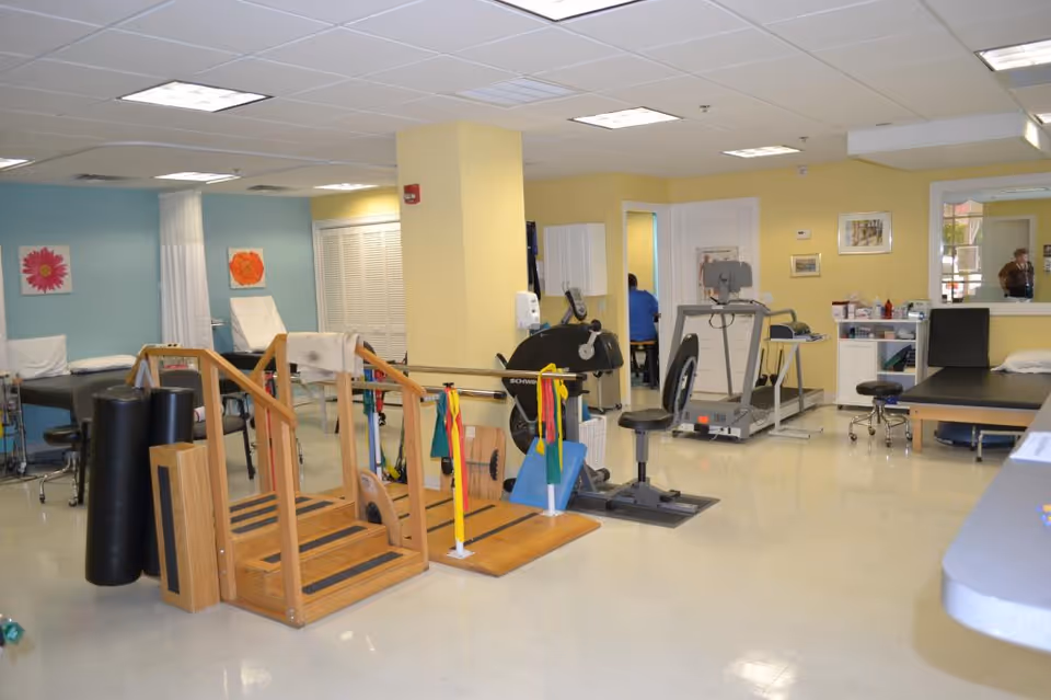 Bright rehab gym featuring parallel bars, treadmills, exercise bikes, and therapy beds.