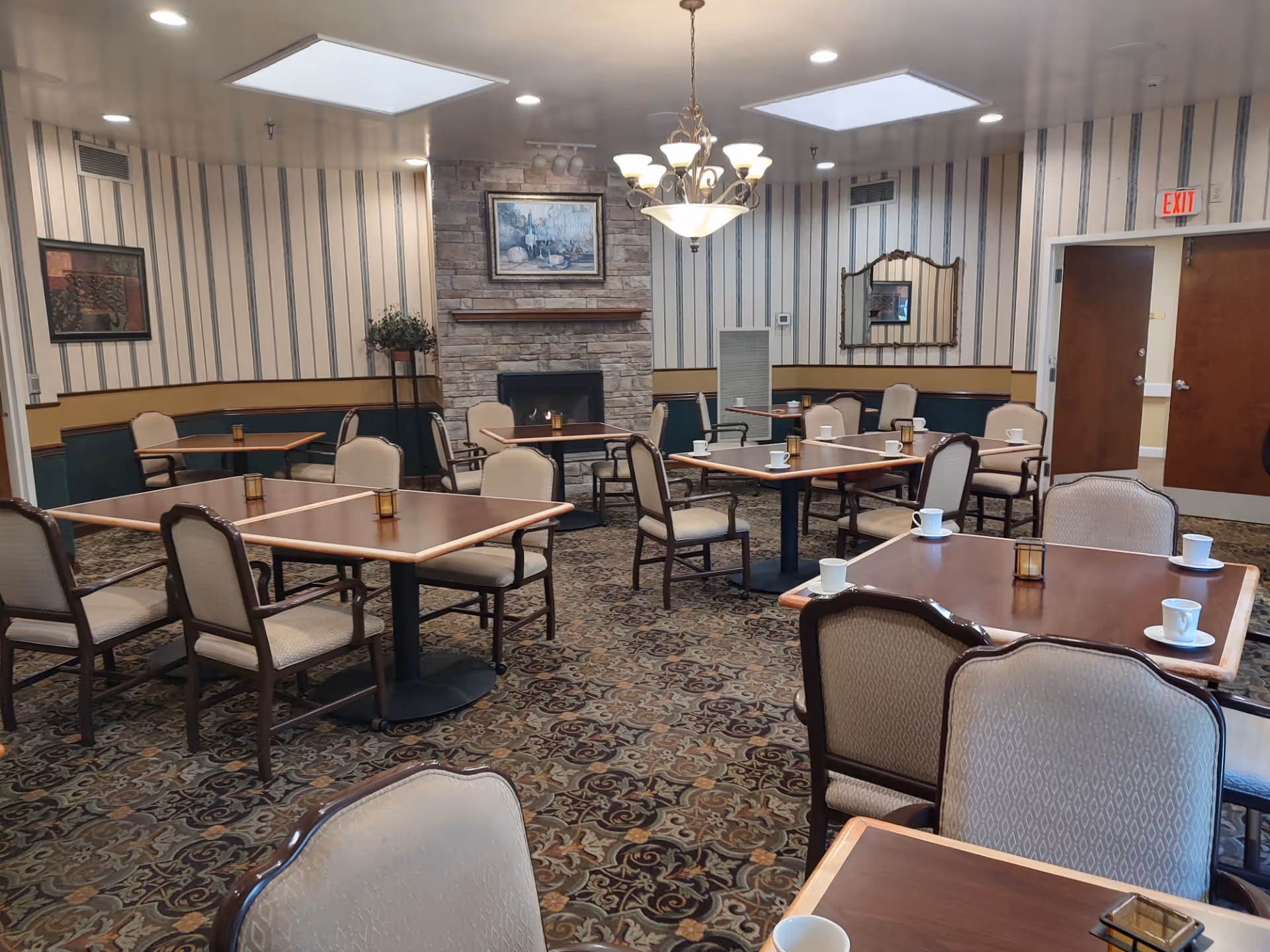 Dining room with multiple tables, beige chairs, patterned carpet, and a stone fireplace.