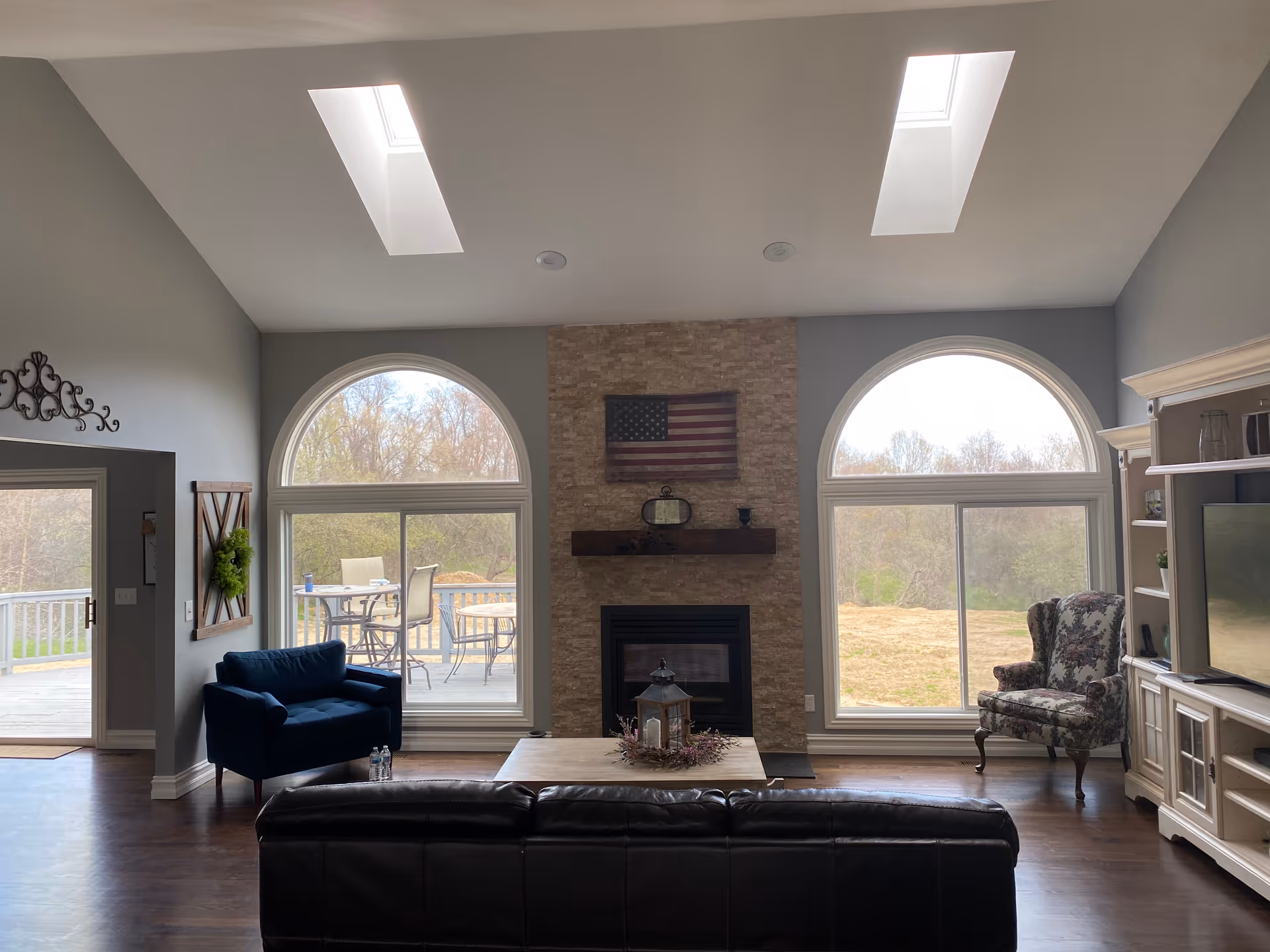 Spacious living room with a stone fireplace, arched windows, and skylights.