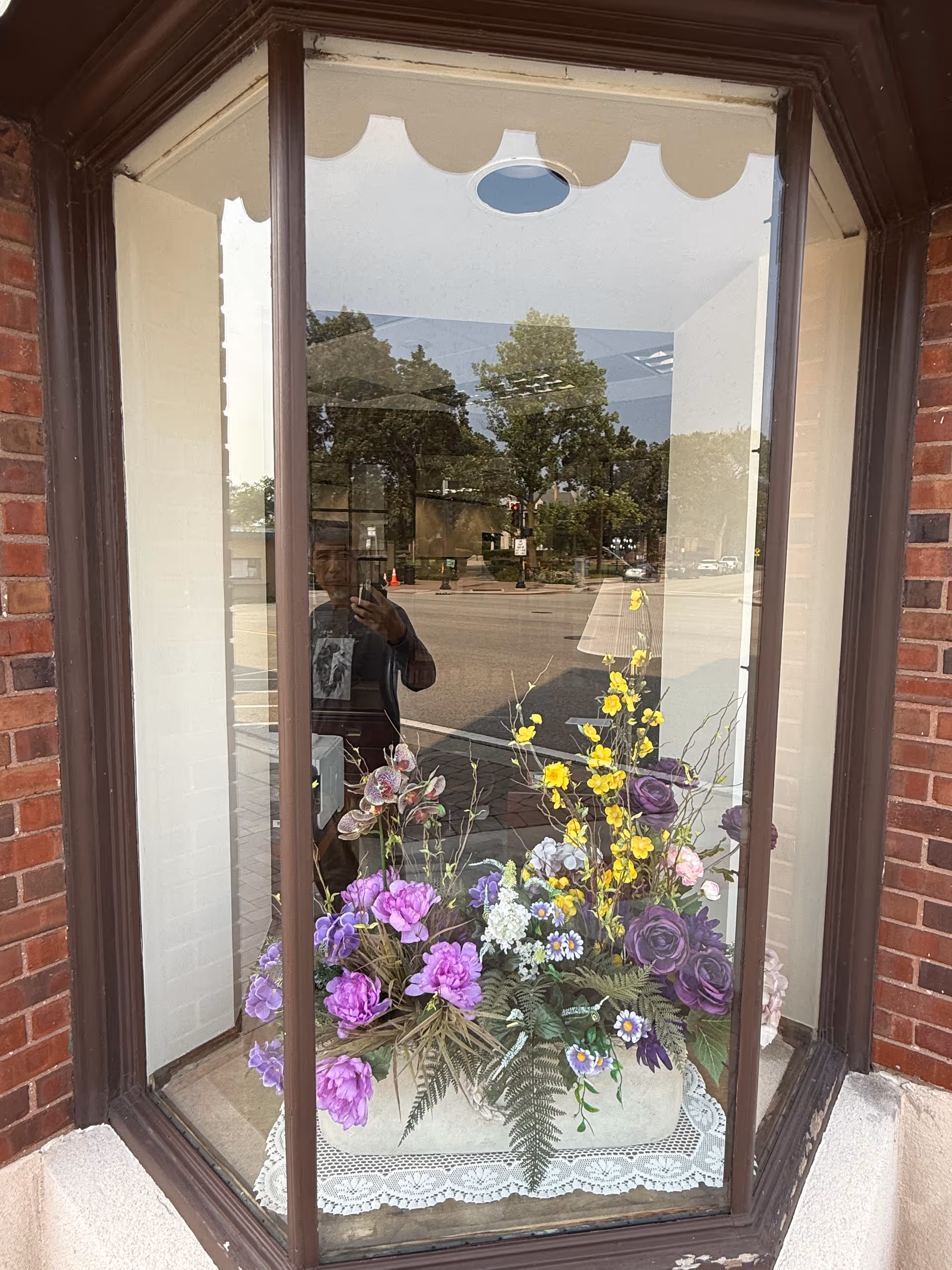 A storefront window display with colorful flowers reflecting the street.
