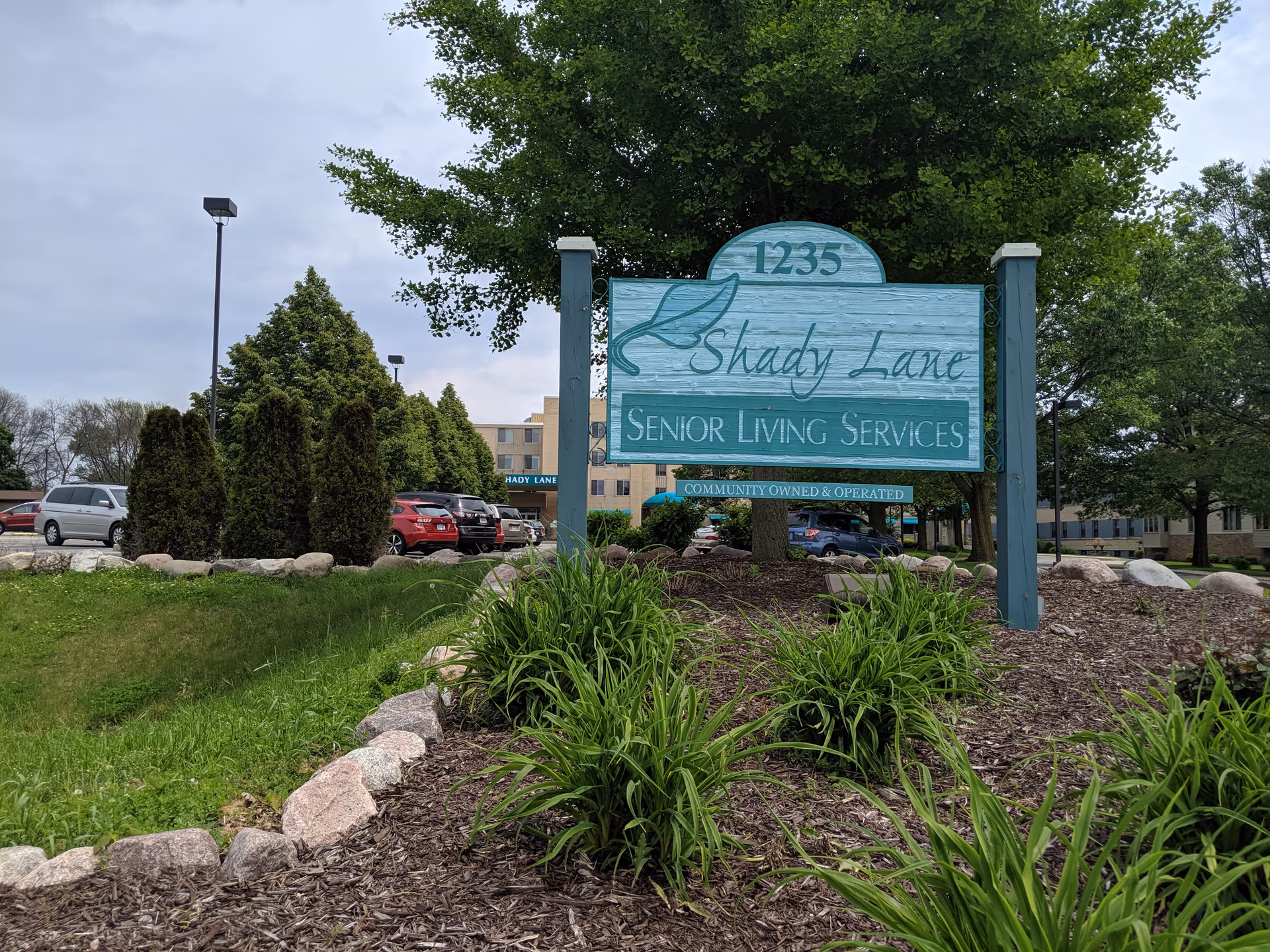 Shady Lane Senior Living Services sign with landscaping and parked cars outside.