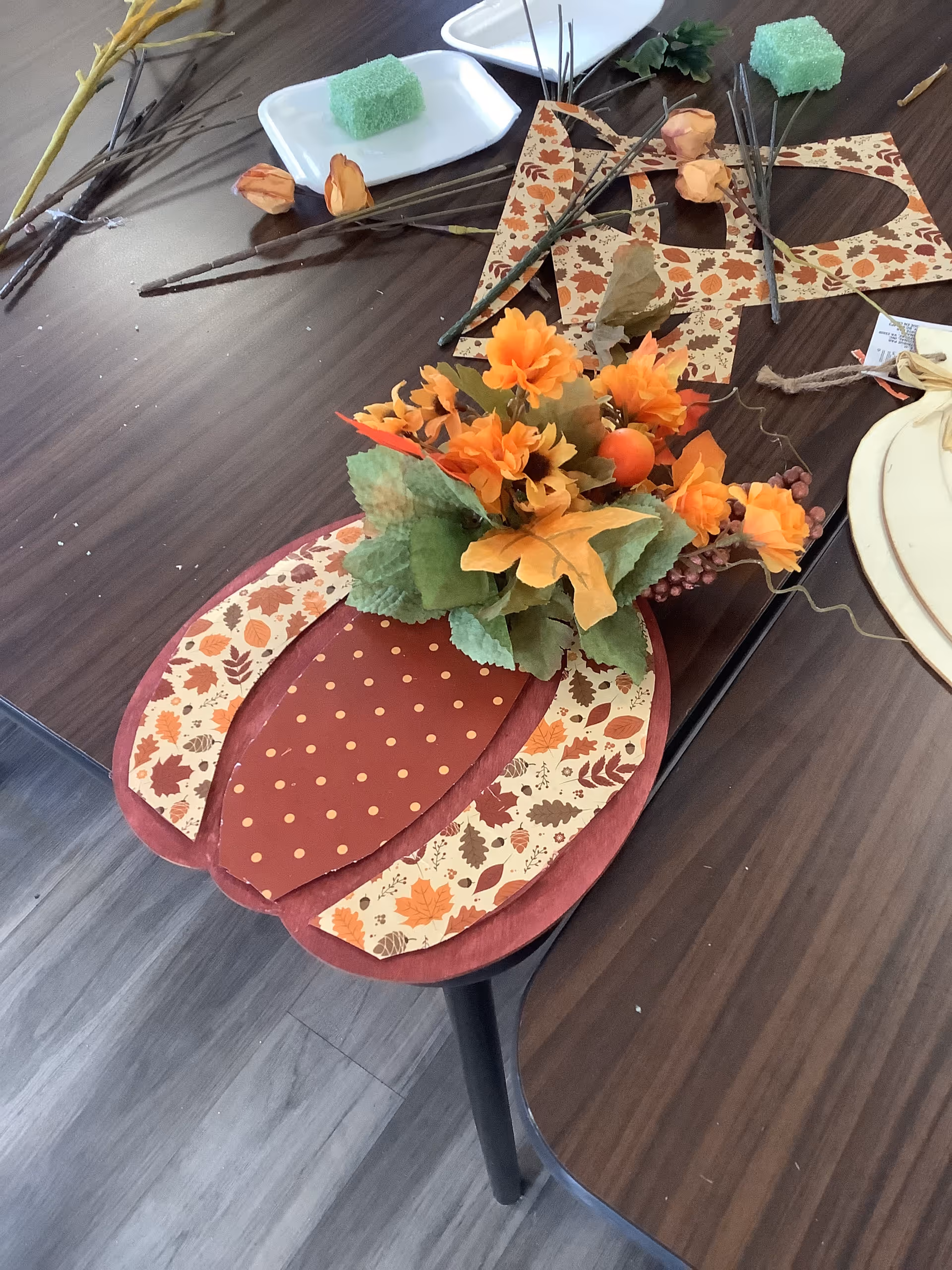 Autumn-themed centerpiece sits on a dining table with plates and leaves.