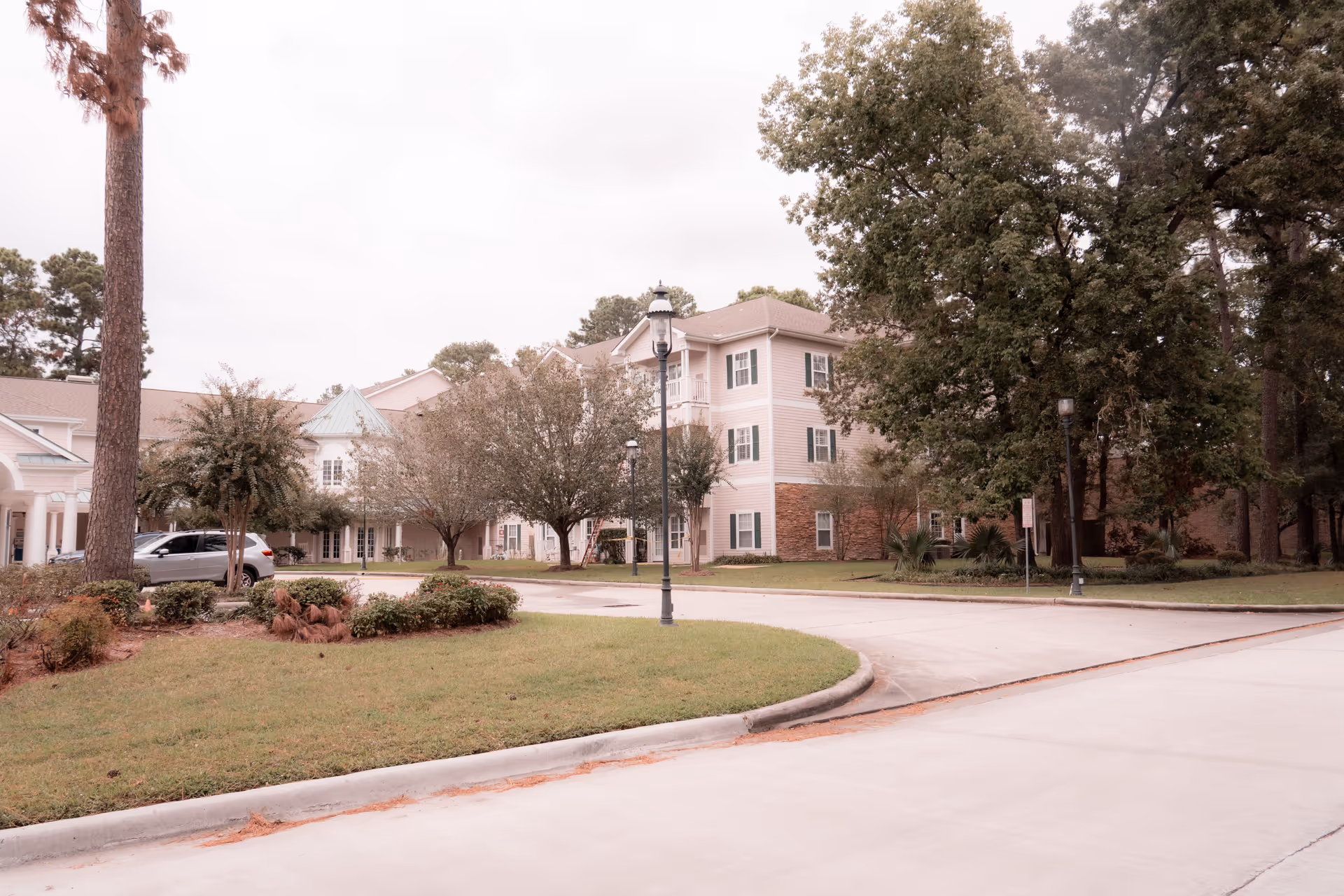 Front exterior of a multi-story senior living building with trees, a circular driveway, and lamp posts.