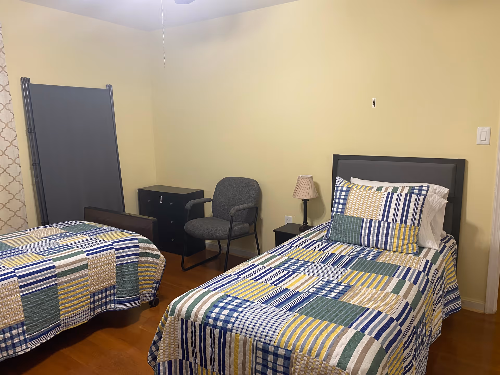 Two twin beds with patchwork quilts, nightstands, a chair, and a dresser in a yellow bedroom.