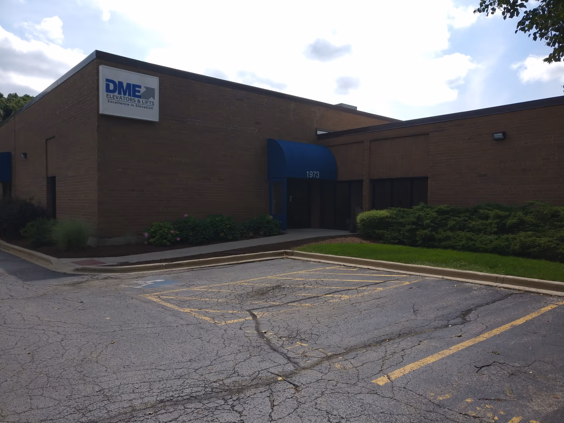 Brick facility with DME Elevators and Lifts sign, blue entrance awning, and surrounding parking lot.