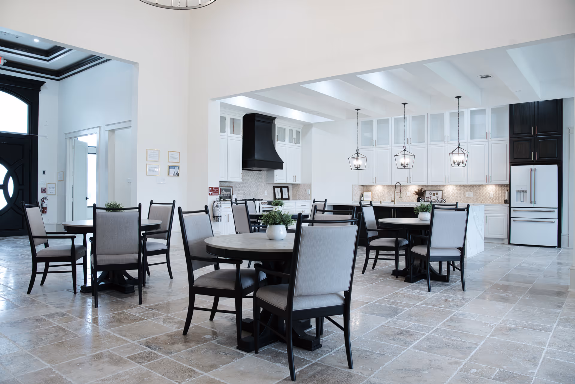 Bright dining area with round tables, chairs, and a modern white kitchen in background.