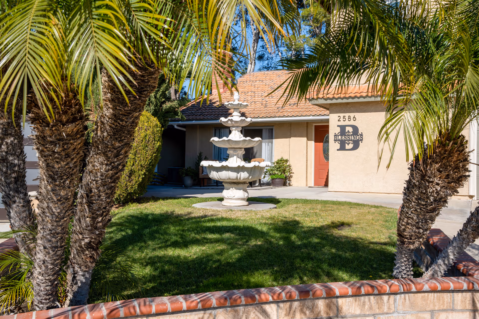 Front view of Blessings Senior Care #2, with a fountain, palm trees, and a beige entrance.