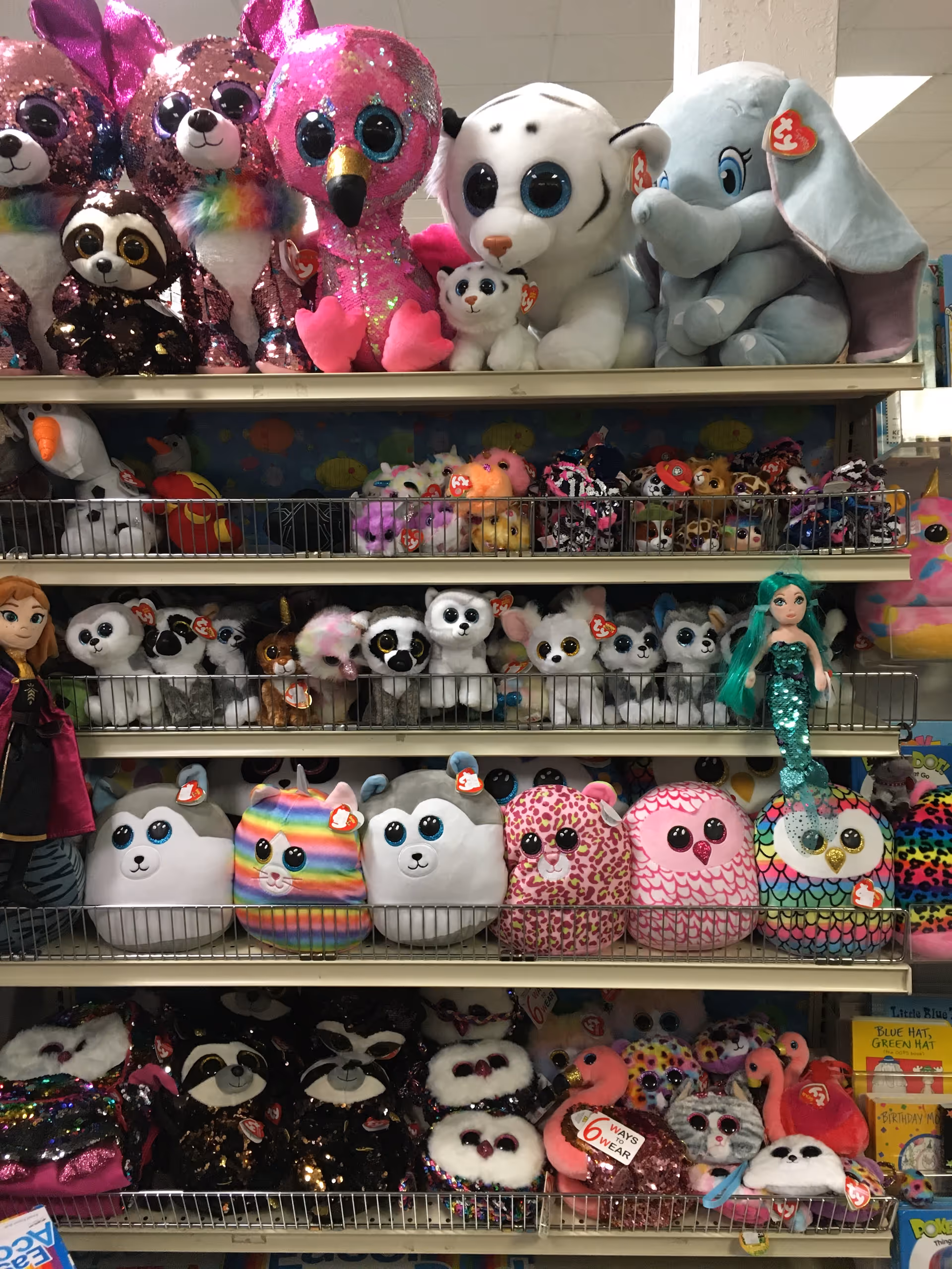 Row of colorful stuffed animals and plush toys displayed on metal shelves.