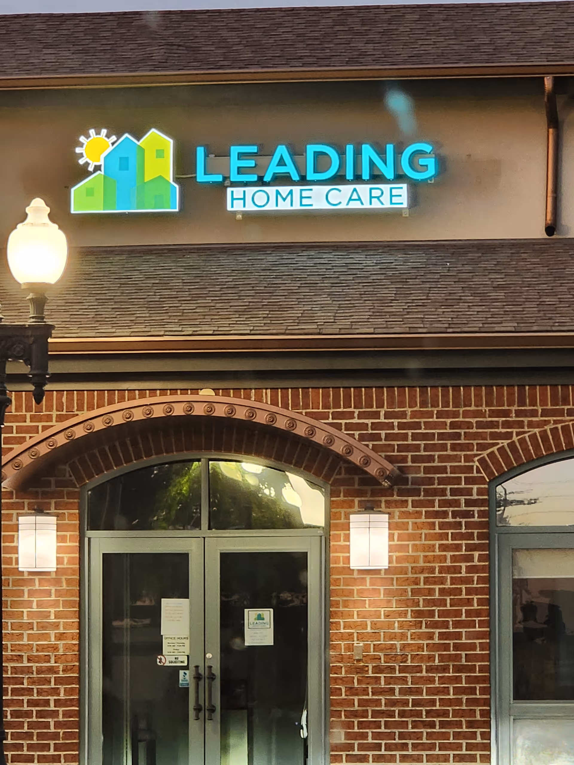 Front exterior of Leading Home Care Monroe with brick facade and illuminated sign.