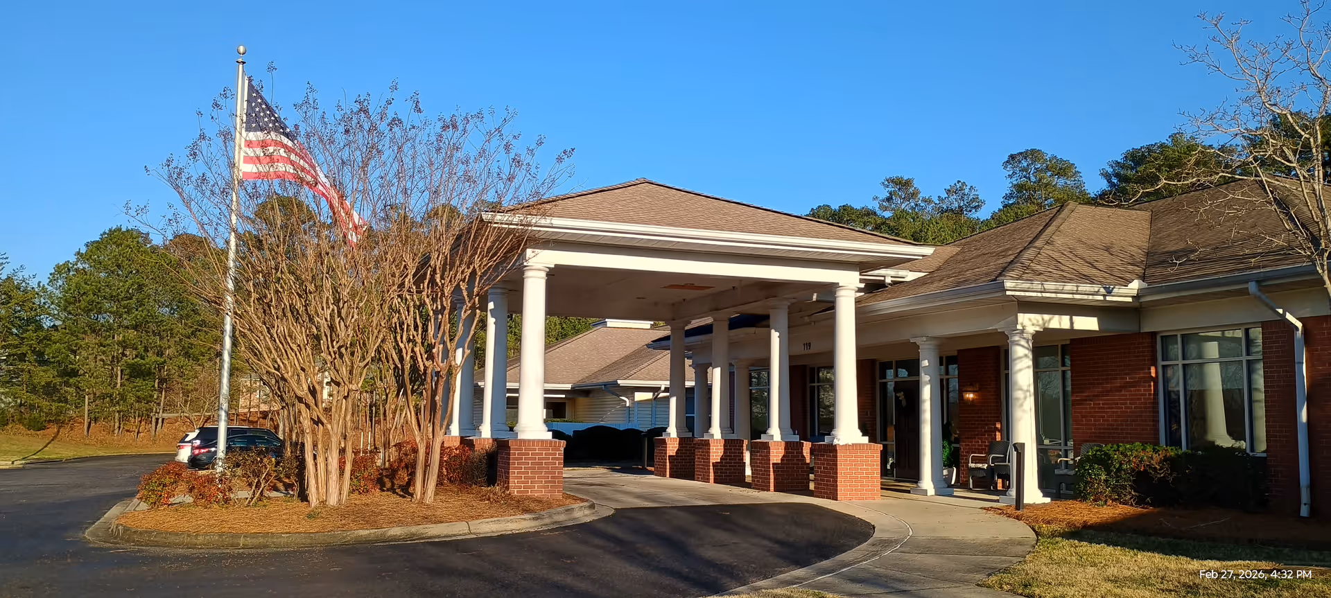 Front entrance of a senior living facility with porte-cochere, brick columns, and a flag.