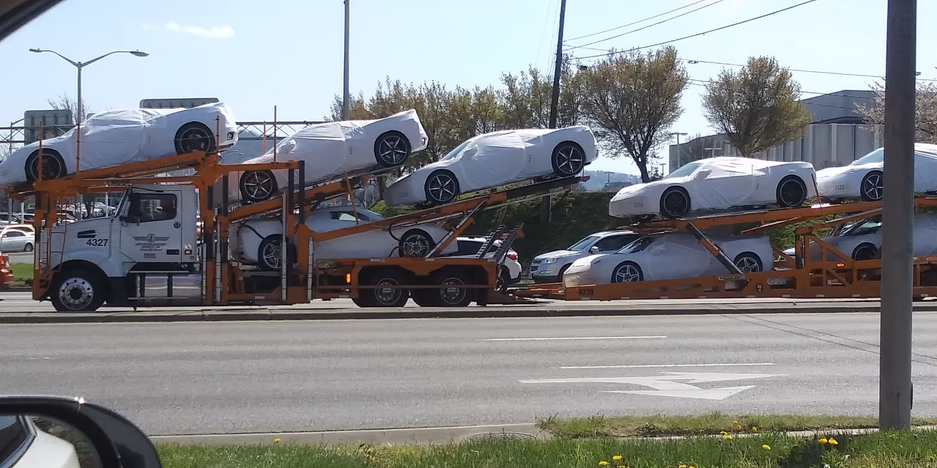 An orange car carrier truck transports several white-covered cars along a busy road.
