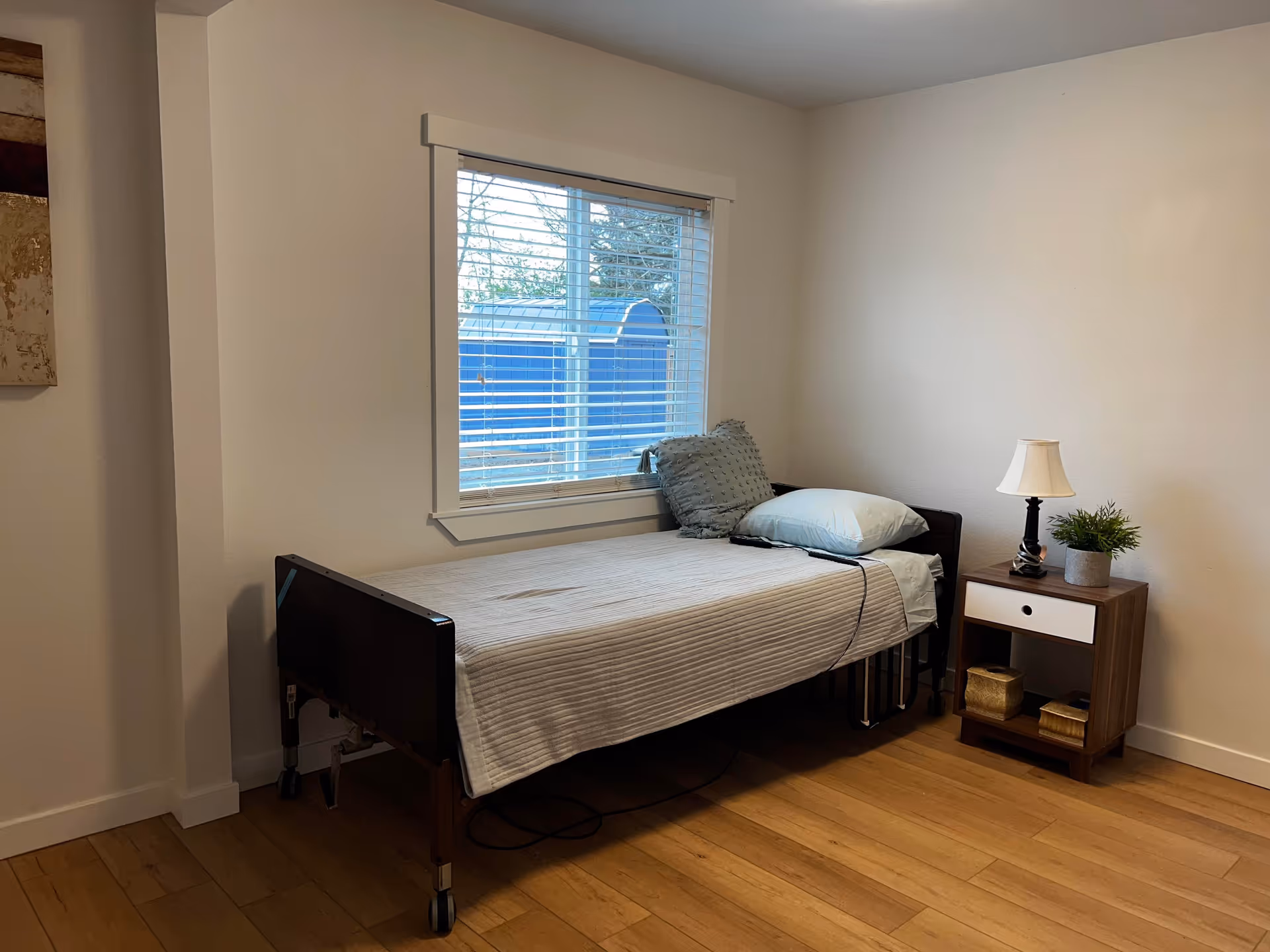 Bedroom with a bed, nightstand, lamp, and window in a neutral minimalist room.