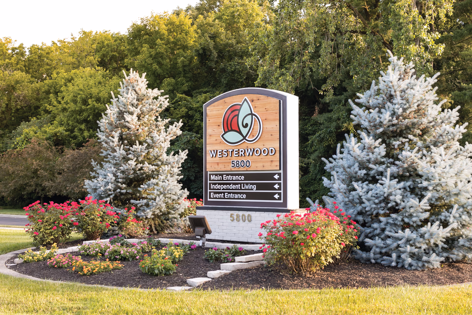 A Westerwood facility sign surrounded by colorful flowers and evergreens at the entrance.